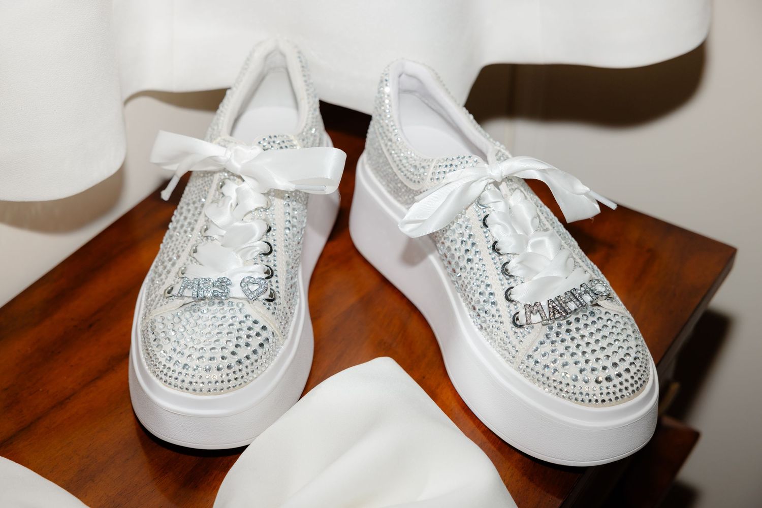 Close-up of rhinestone-encrusted white platform sneakers with laces on wooden surface.