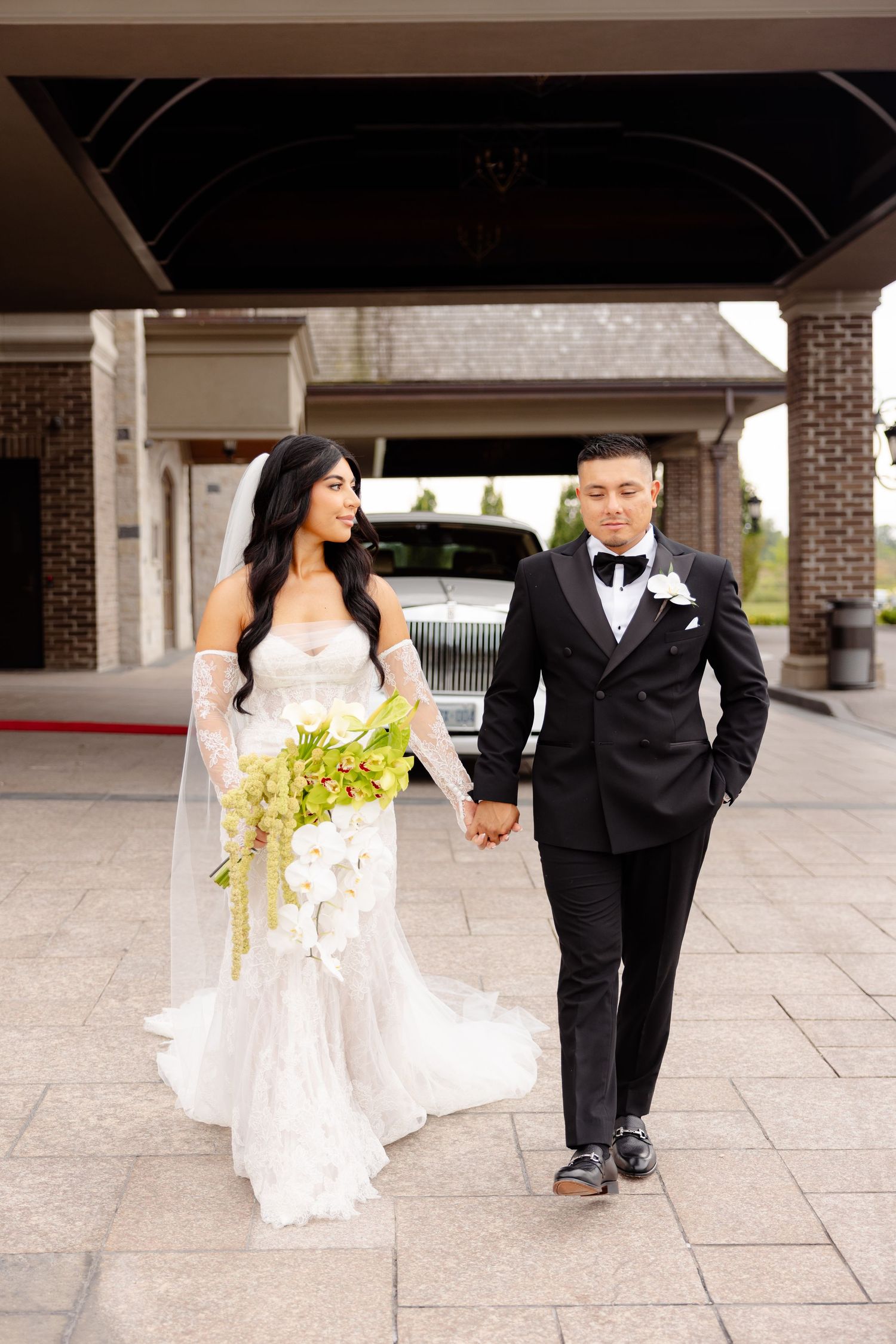 A wedding couple walks together on a stone patio in elegant wedding attire on their special day.