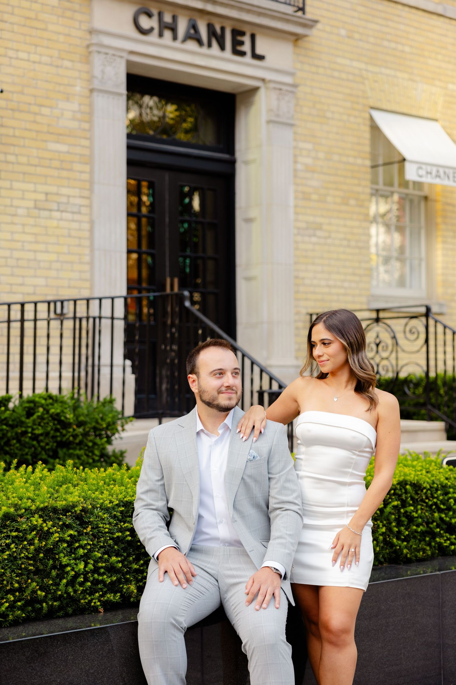 Fashionable pair poses casually outside Chanel store entrance with yellow brick facade.
