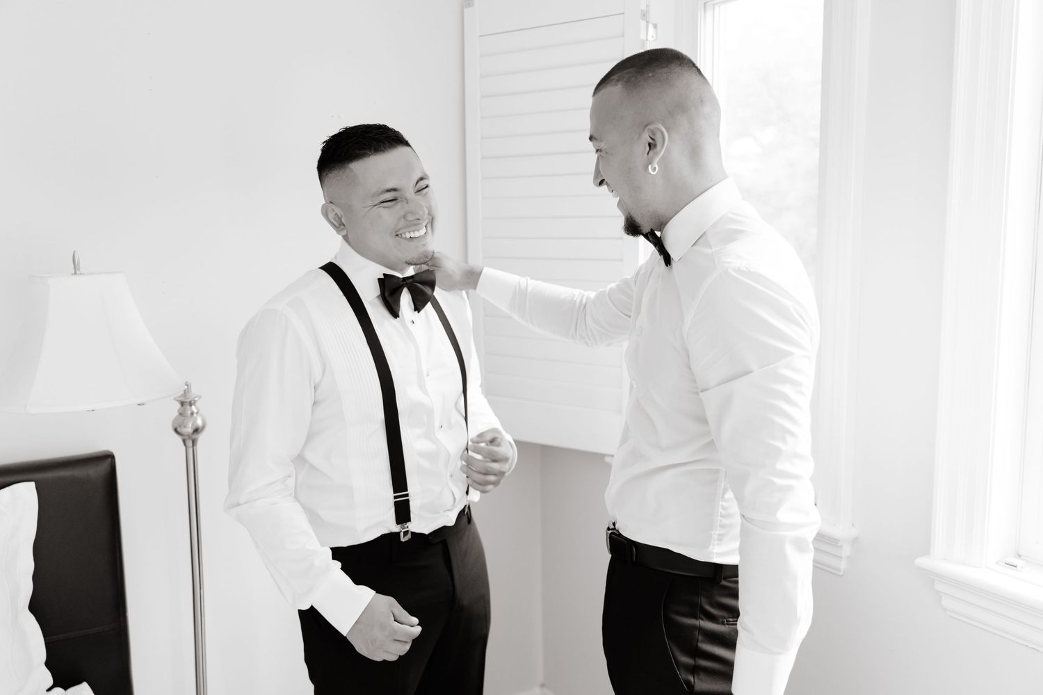 Groomsmen in black tuxedos and white shirts help each other prepare before a wedding ceremony.