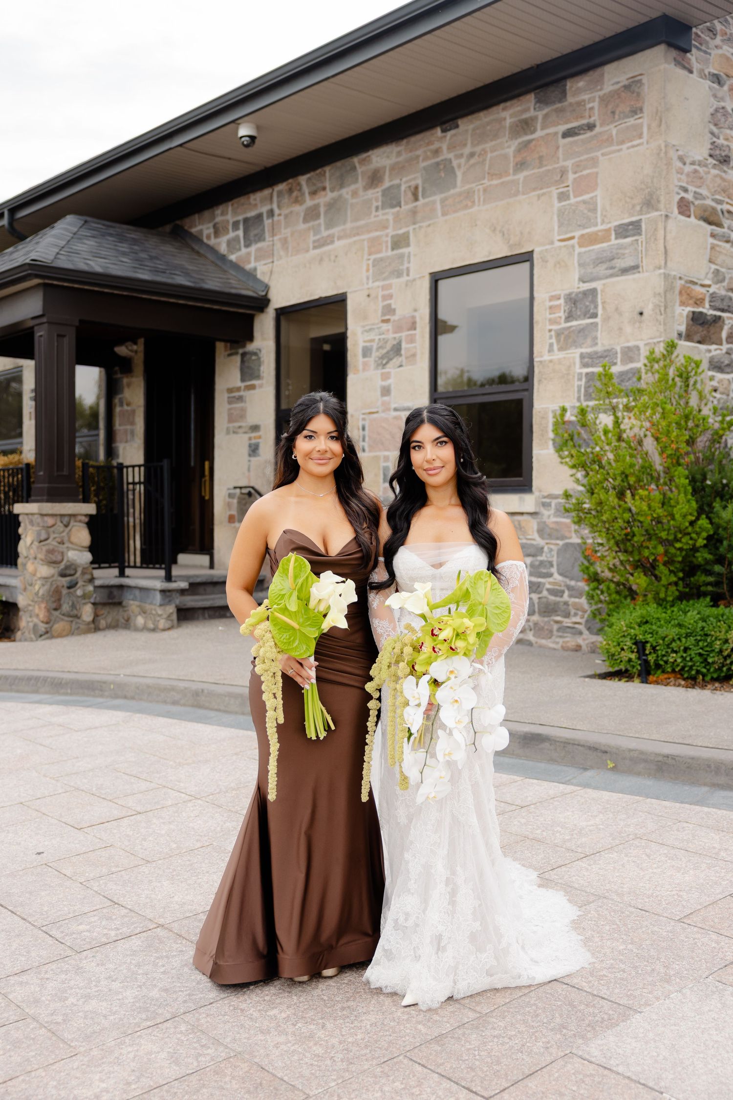 A bridal party wearing brown and white dresses poses on stone steps outside the building entrance.