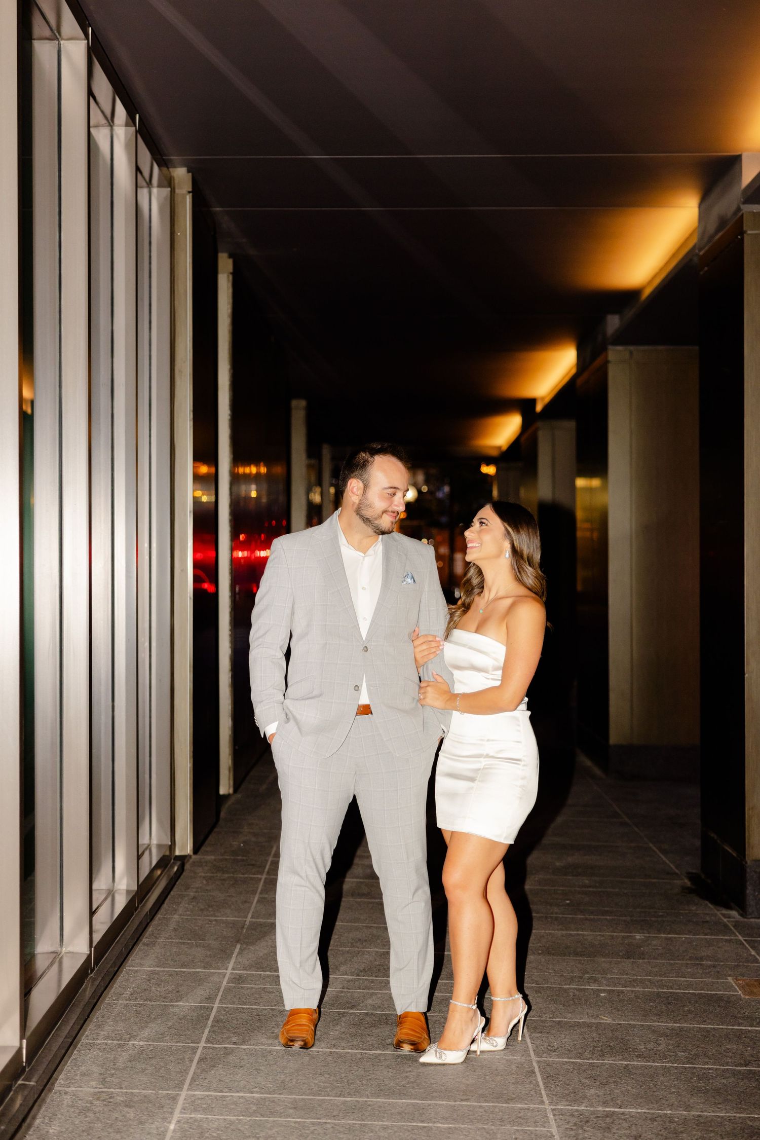 Stylish couple sharing an intimate moment in an illuminated corridor.