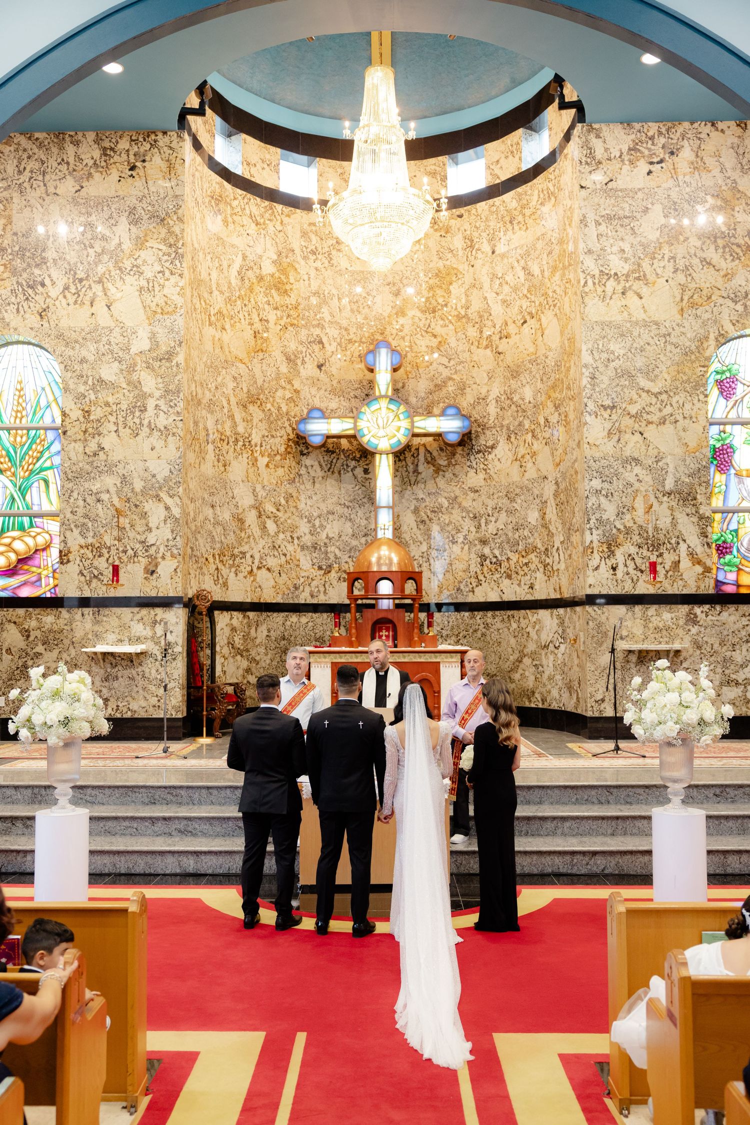 A wedding ceremony setup in a church with ornate decor, stained glass windows, and a large cross at the altar.