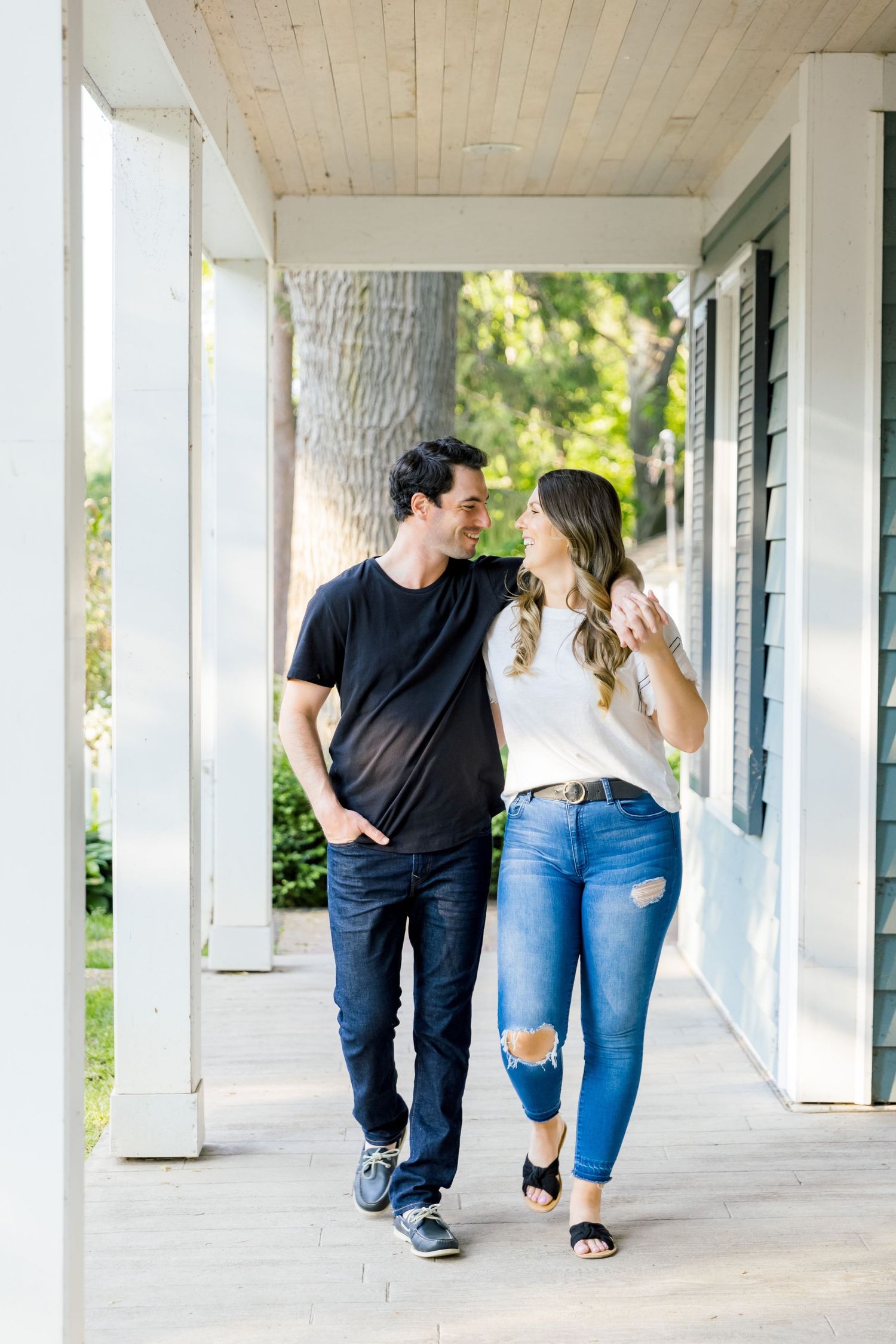 A couple strolls together on a covered porch with white columns in casual summer attire.