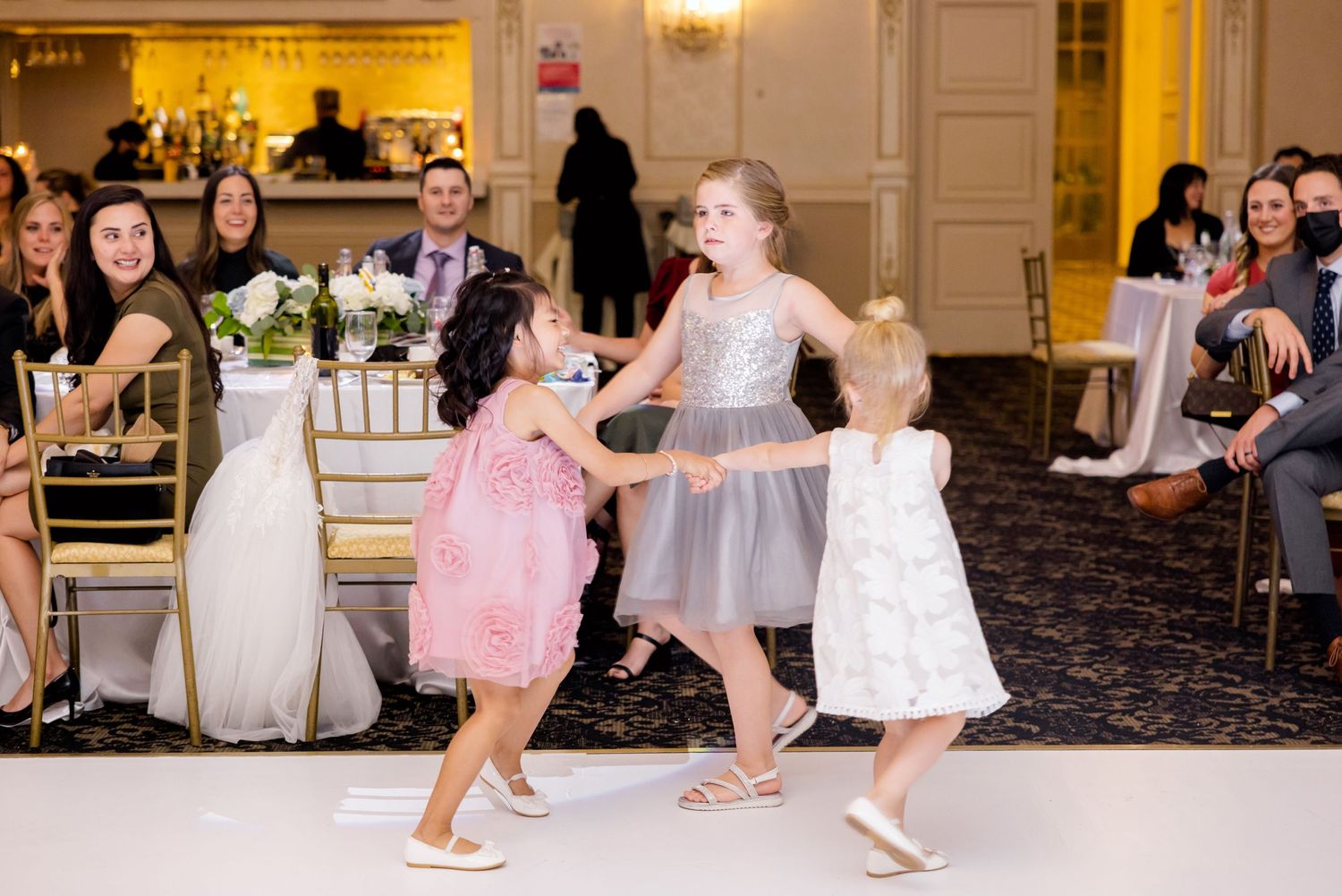 Young children in party dresses dancing and twirling on a wedding reception dance floor.