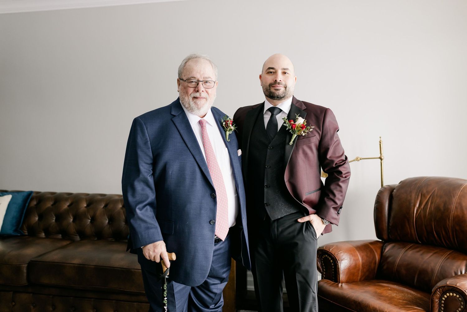 Two people in contrasting suits standing in front of a brown leather couch.