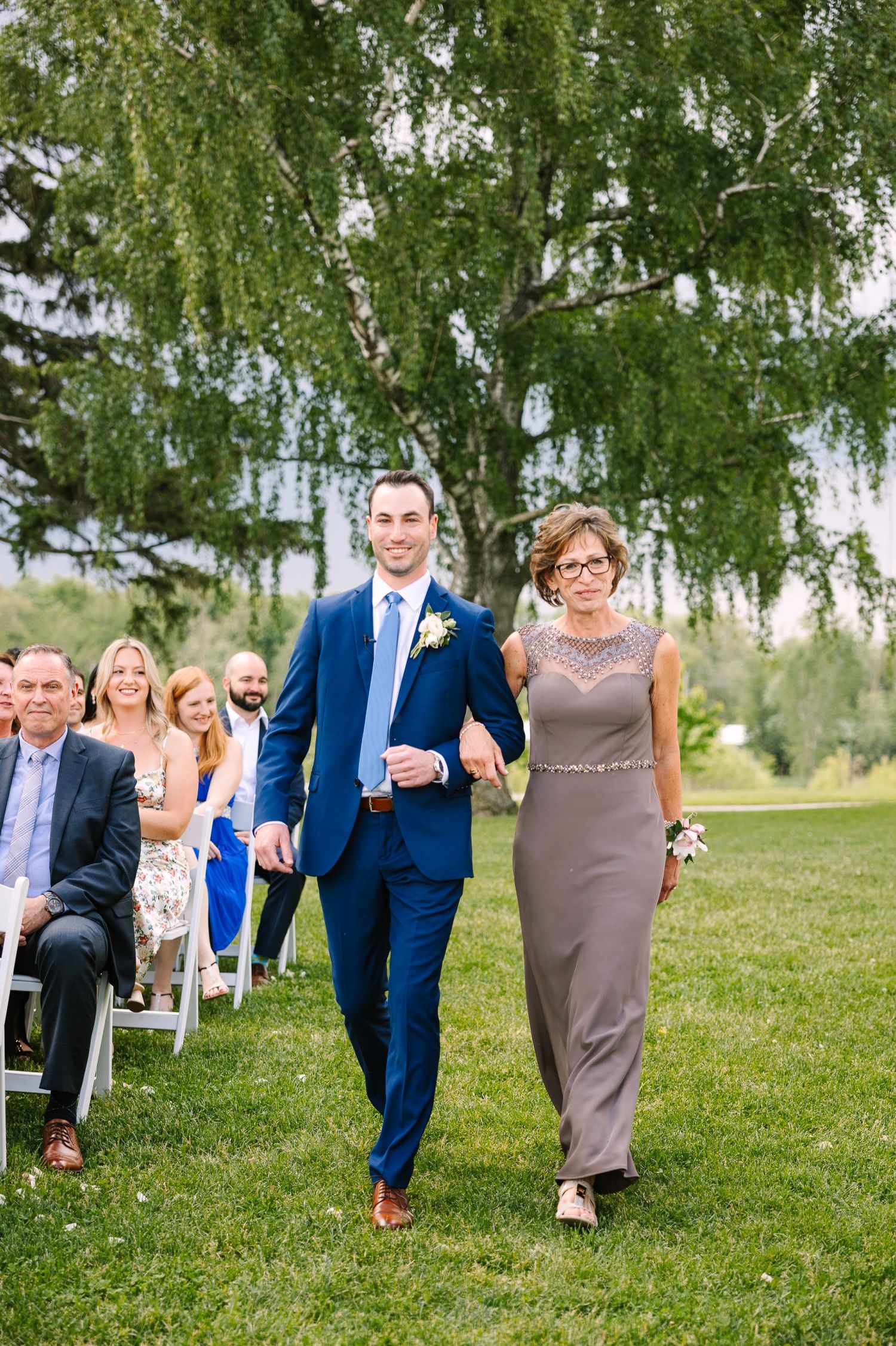 Wedding ceremony processional on green lawn with weeping birch trees in background.