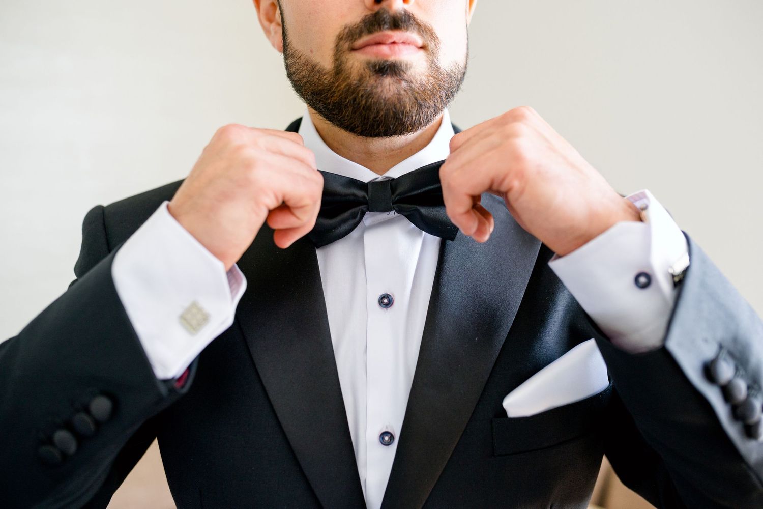Close-up shot of hands adjusting a black bow tie on a formal tuxedo.