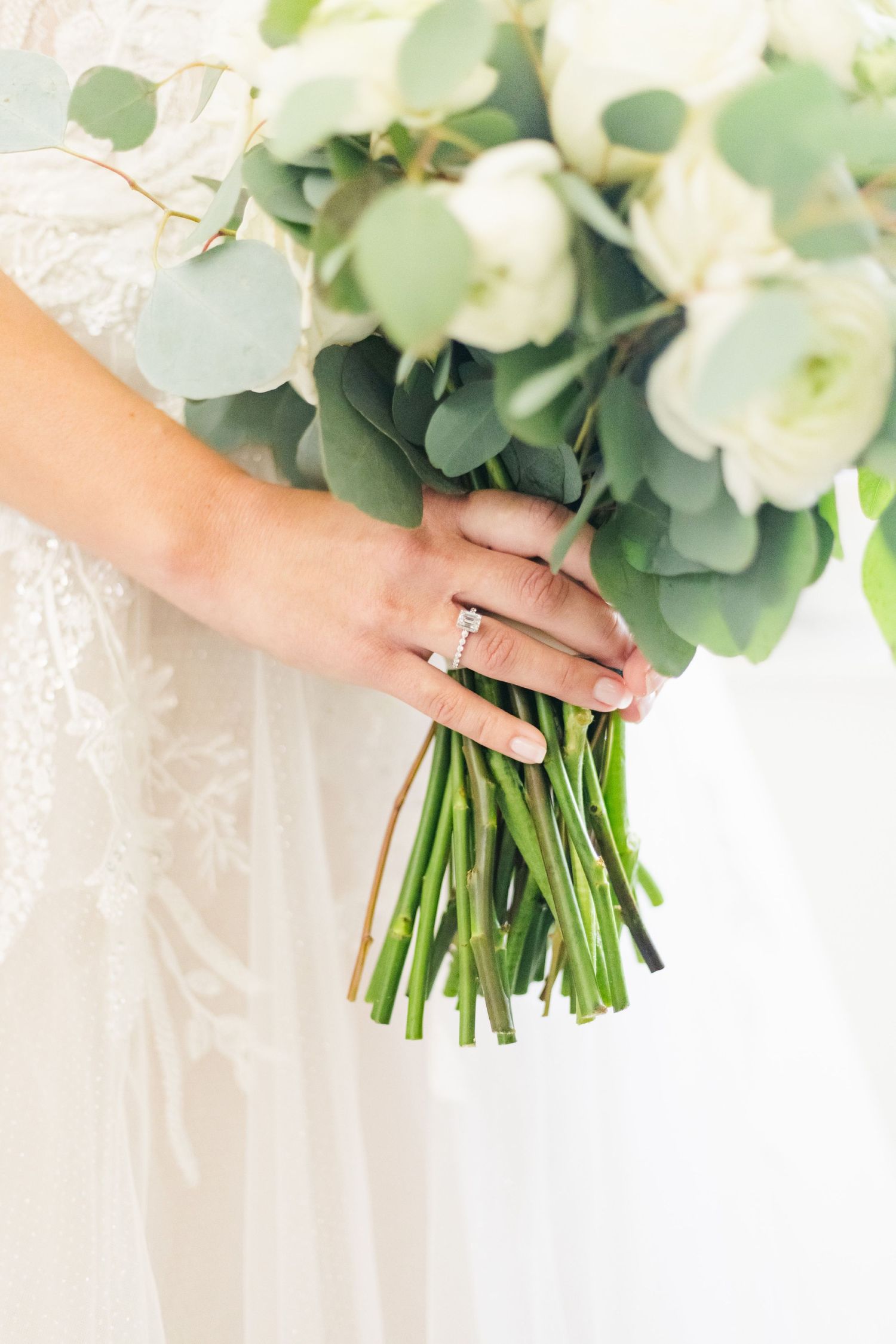 Close up of bridal bouquet with white flowers and engagement ring detail.
