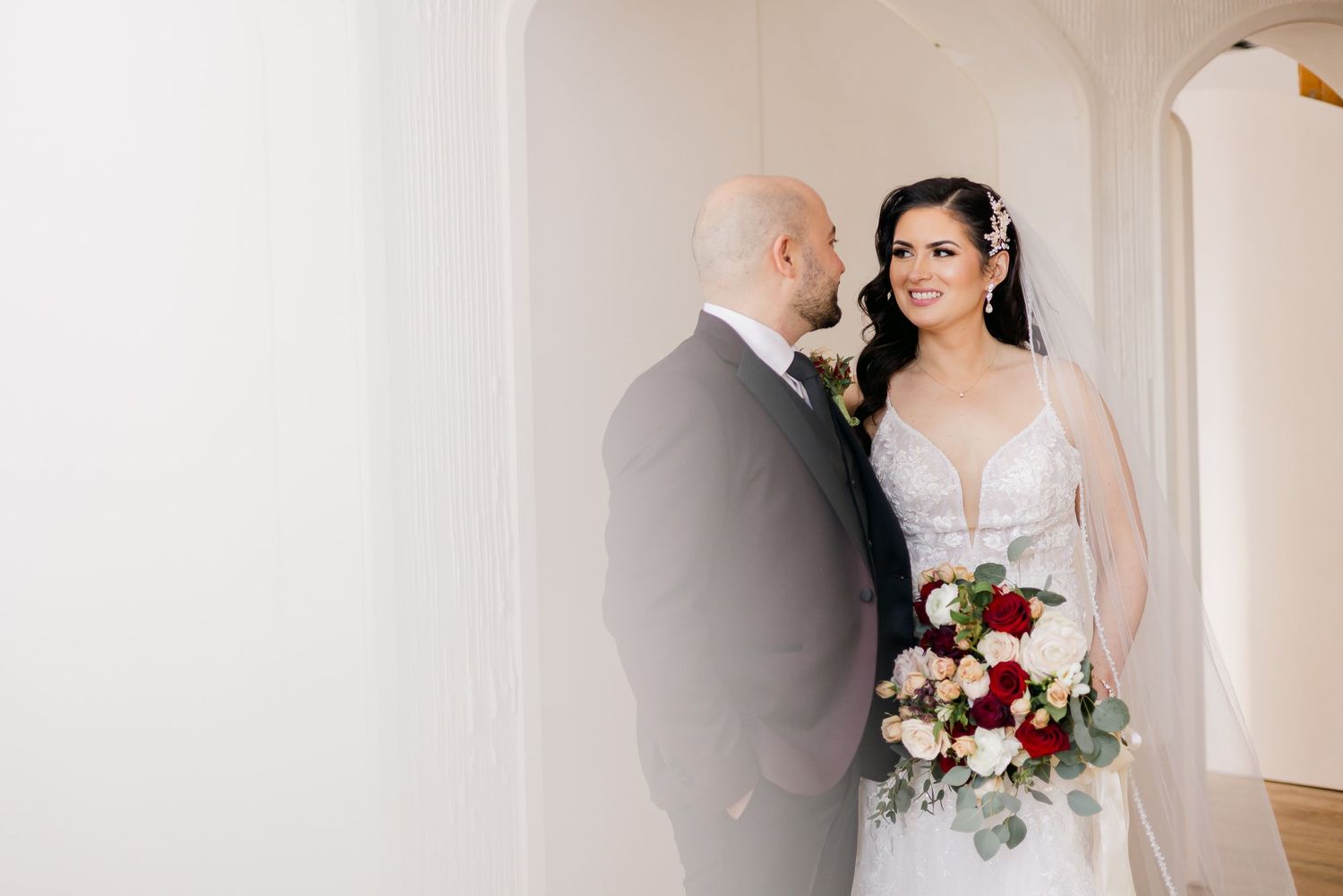 Intimate wedding portrait in front of white archway with burgundy bouquet.