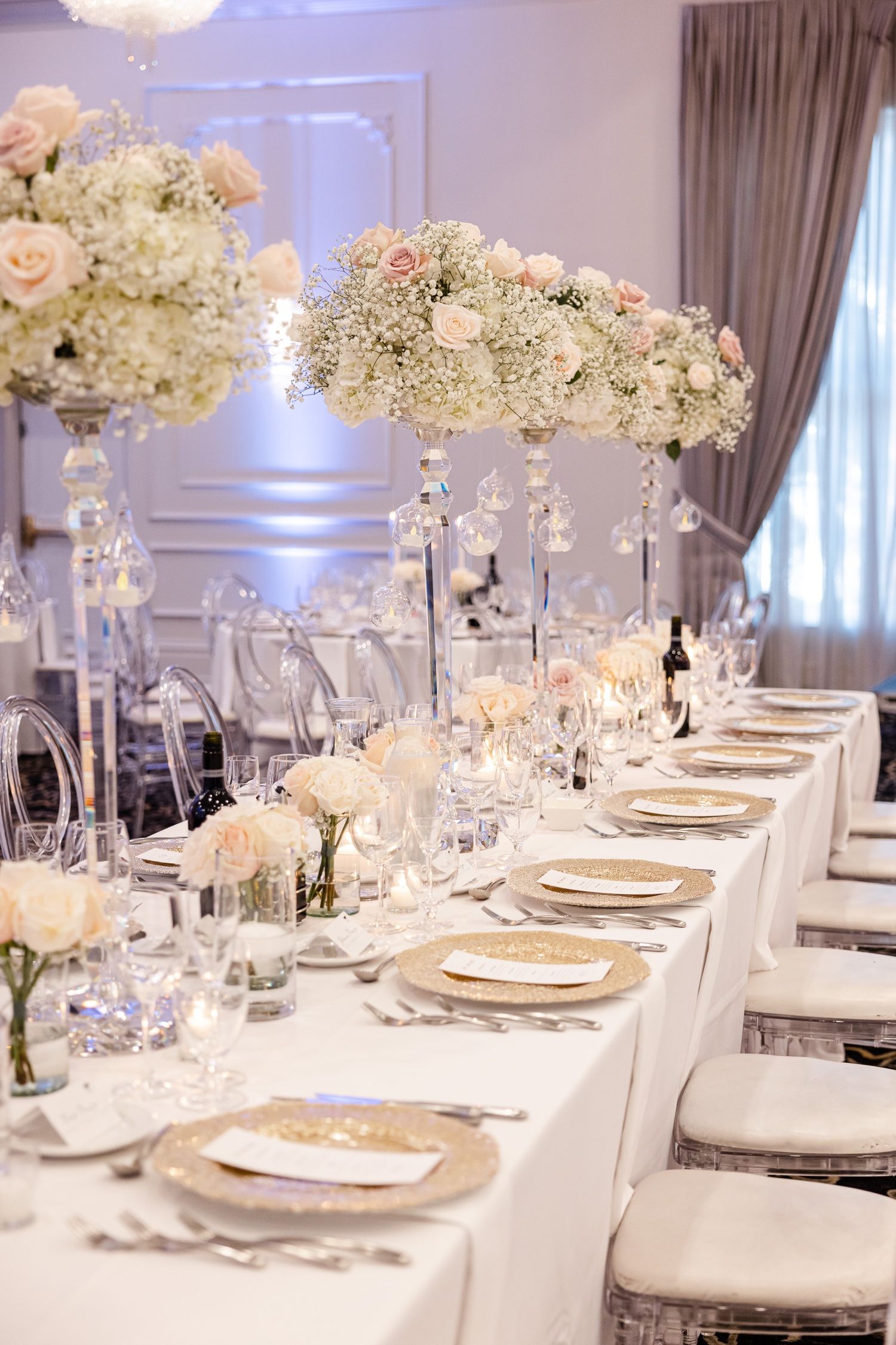 Long banquet table with high crystal centerpieces filled with roses and baby's breath against draped walls.