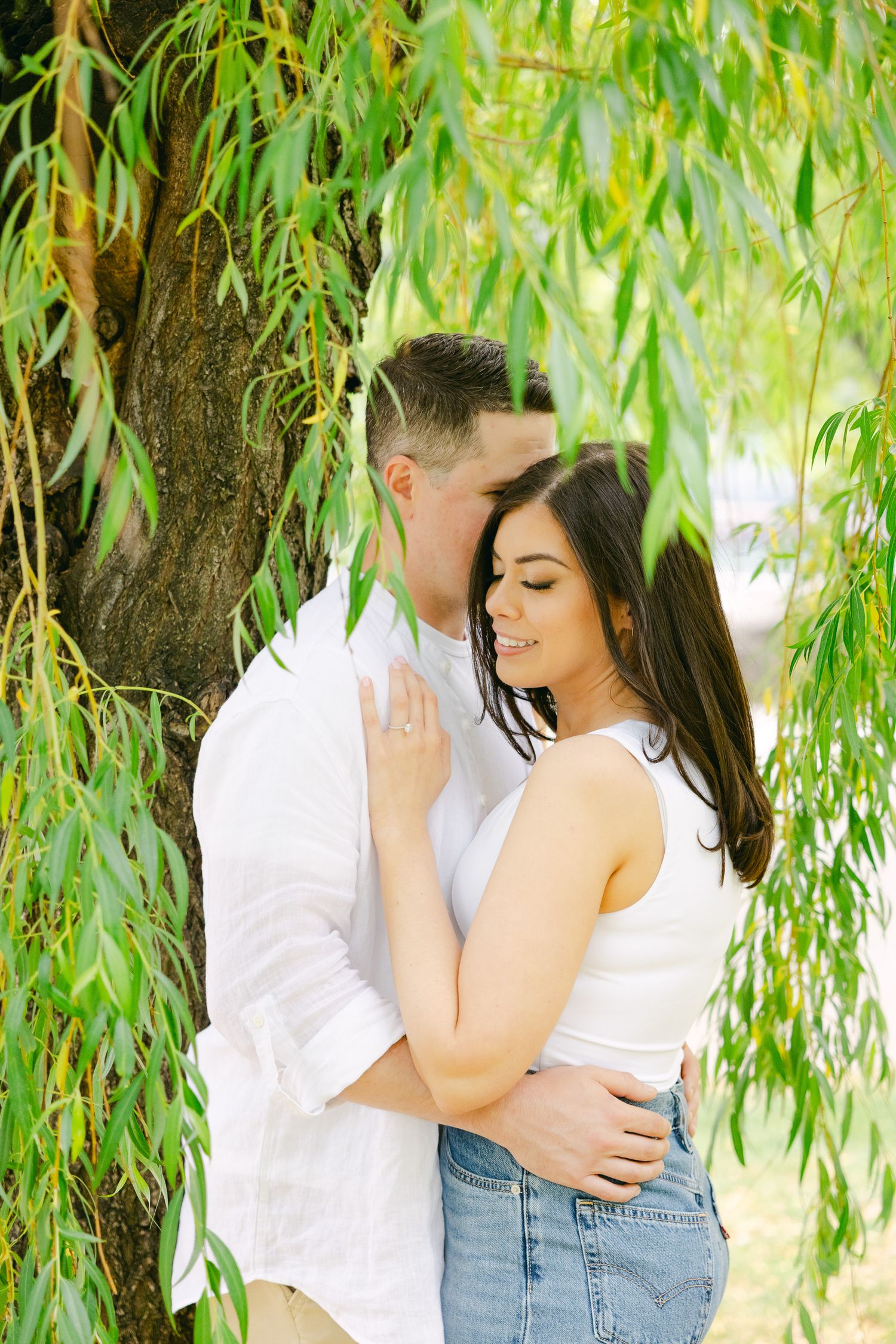 Romantic embrace captured beneath cascading willow branches in sunlit park.