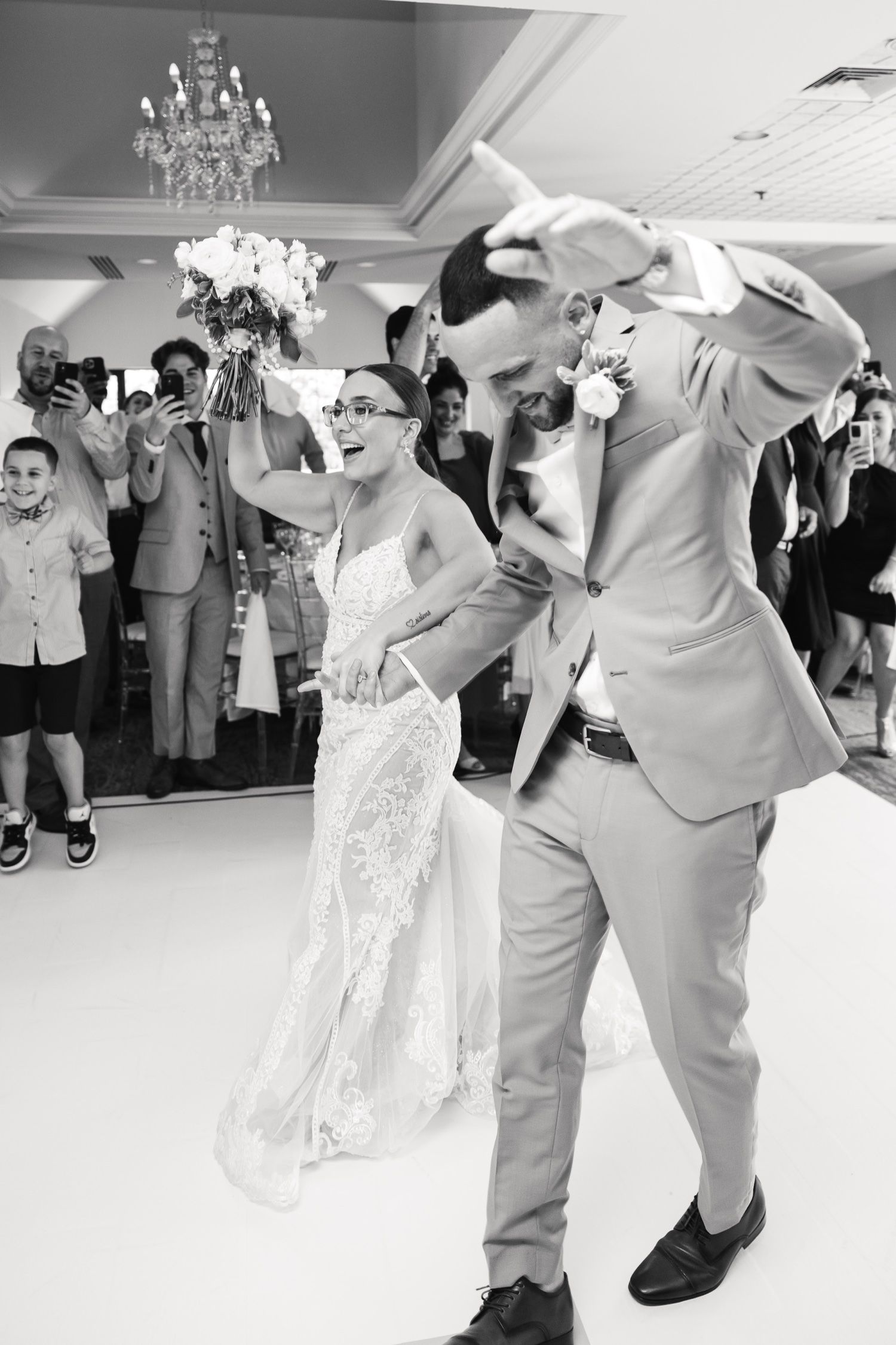 Black and white photo of an energetic wedding dance celebration with guests watching.