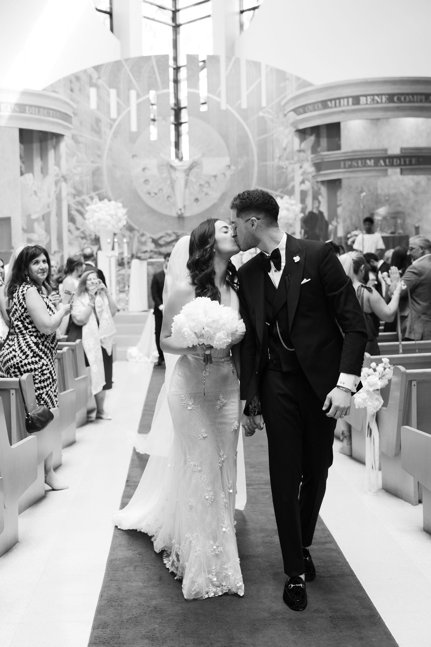 A black and white photo captures a romantic moment between newlyweds on their church exit.