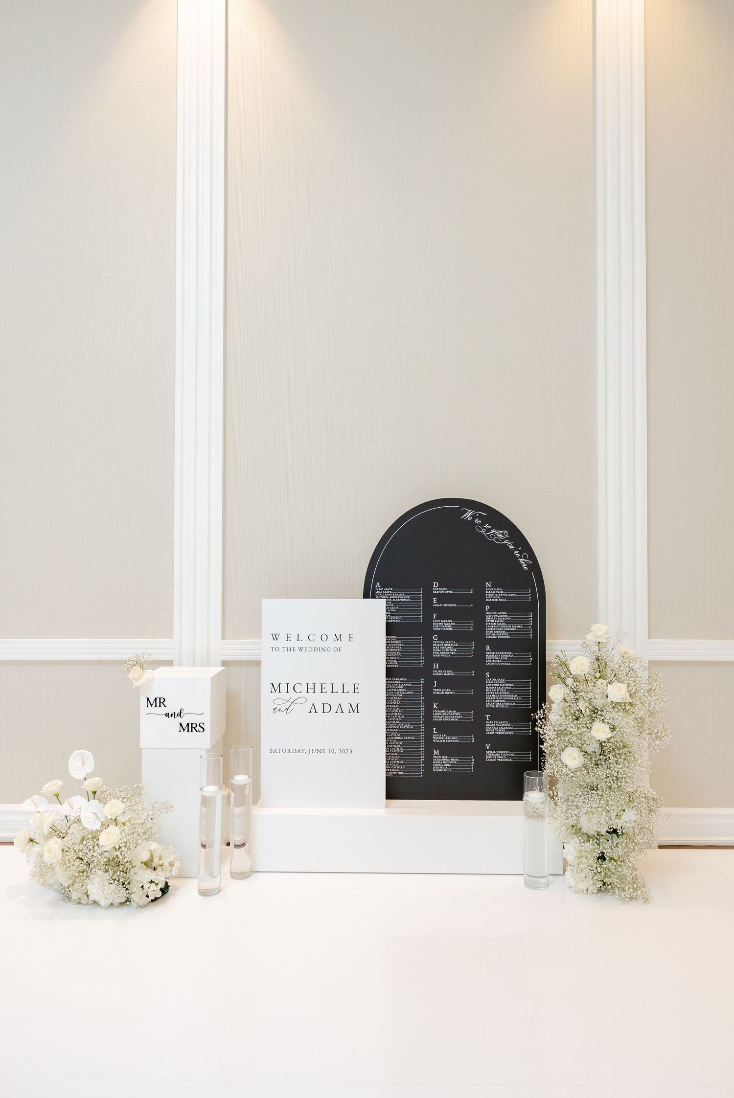 Modern wedding welcome display with seating chart and white floral arrangements.