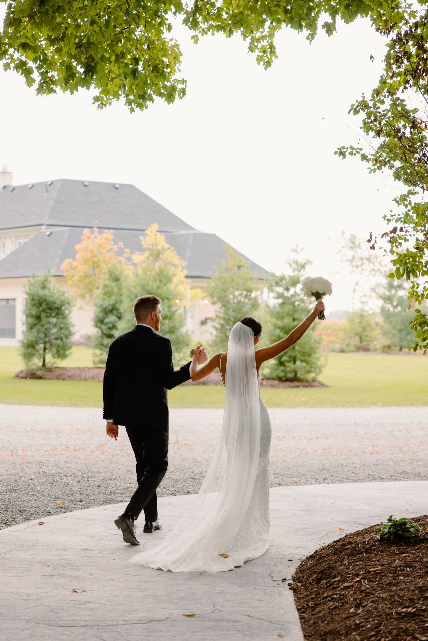 Wedding couple celebrates on path with flowing veil and mountain backdrop.