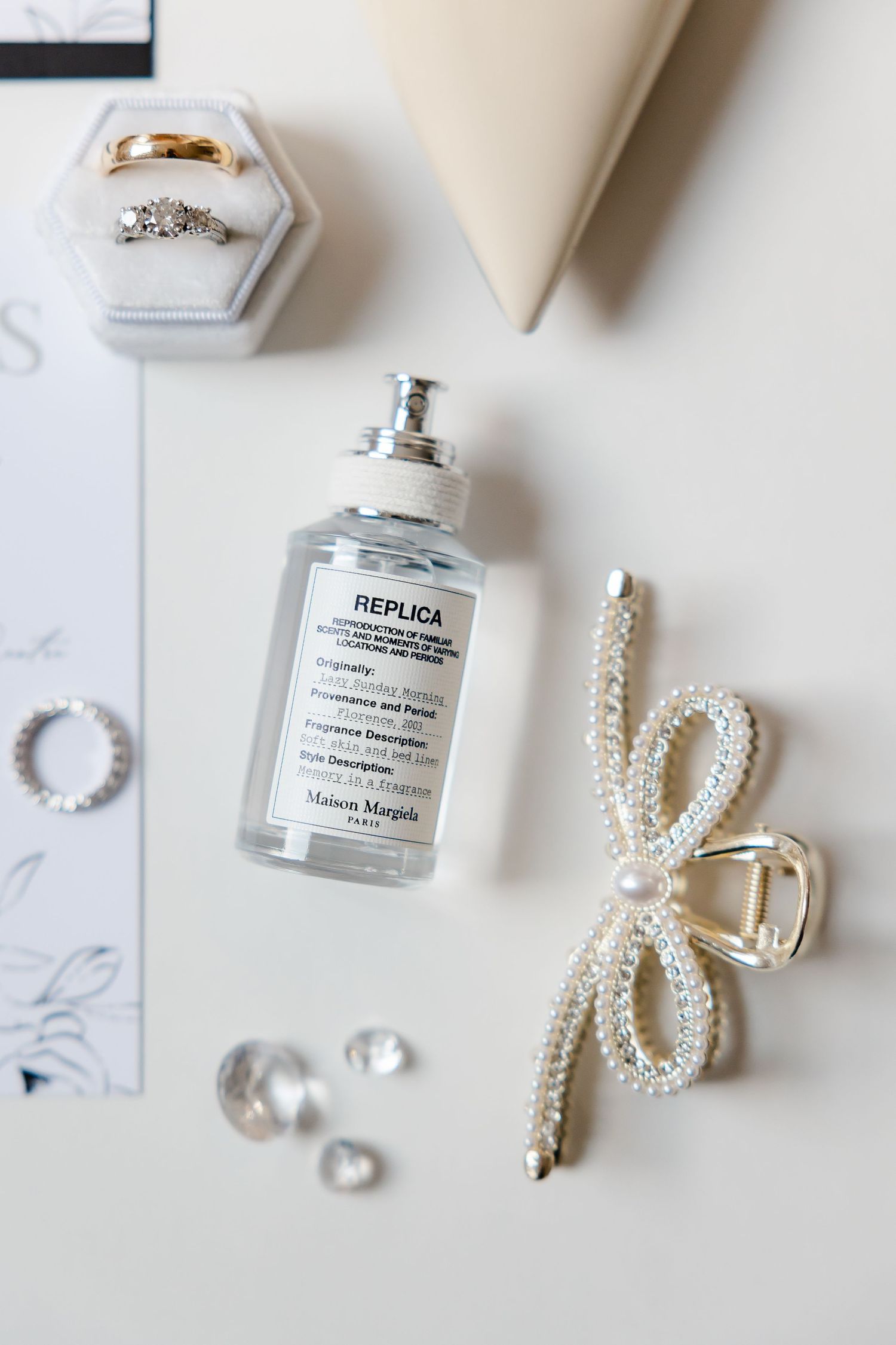 Wedding accessories including perfume bottle, pearl bow hair clip, rings, and jewelry on white surface.