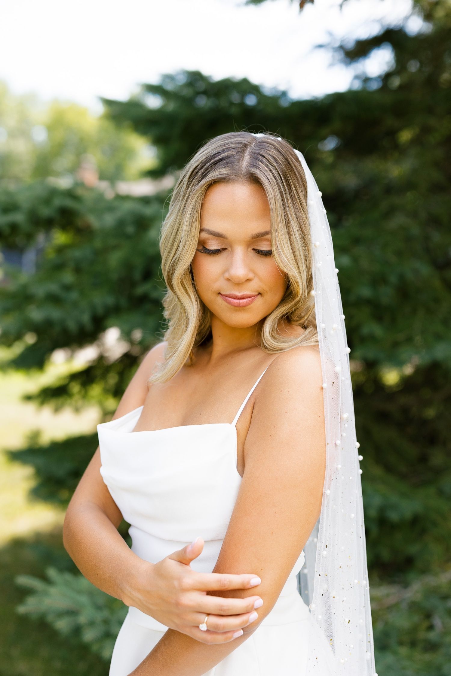 Close-up bridal portrait showcasing delicate veil and natural makeup against green foliage.