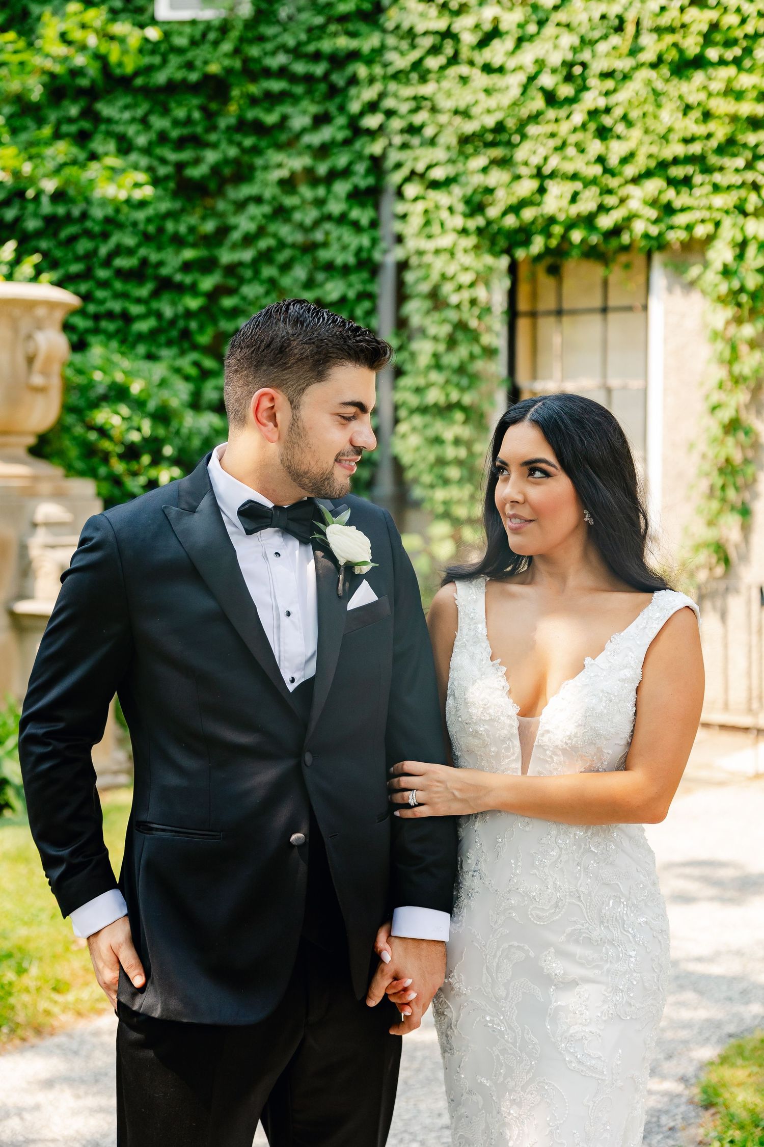 Elegant couple sharing a moment in front of ivy-covered walls in formal wedding attire.
