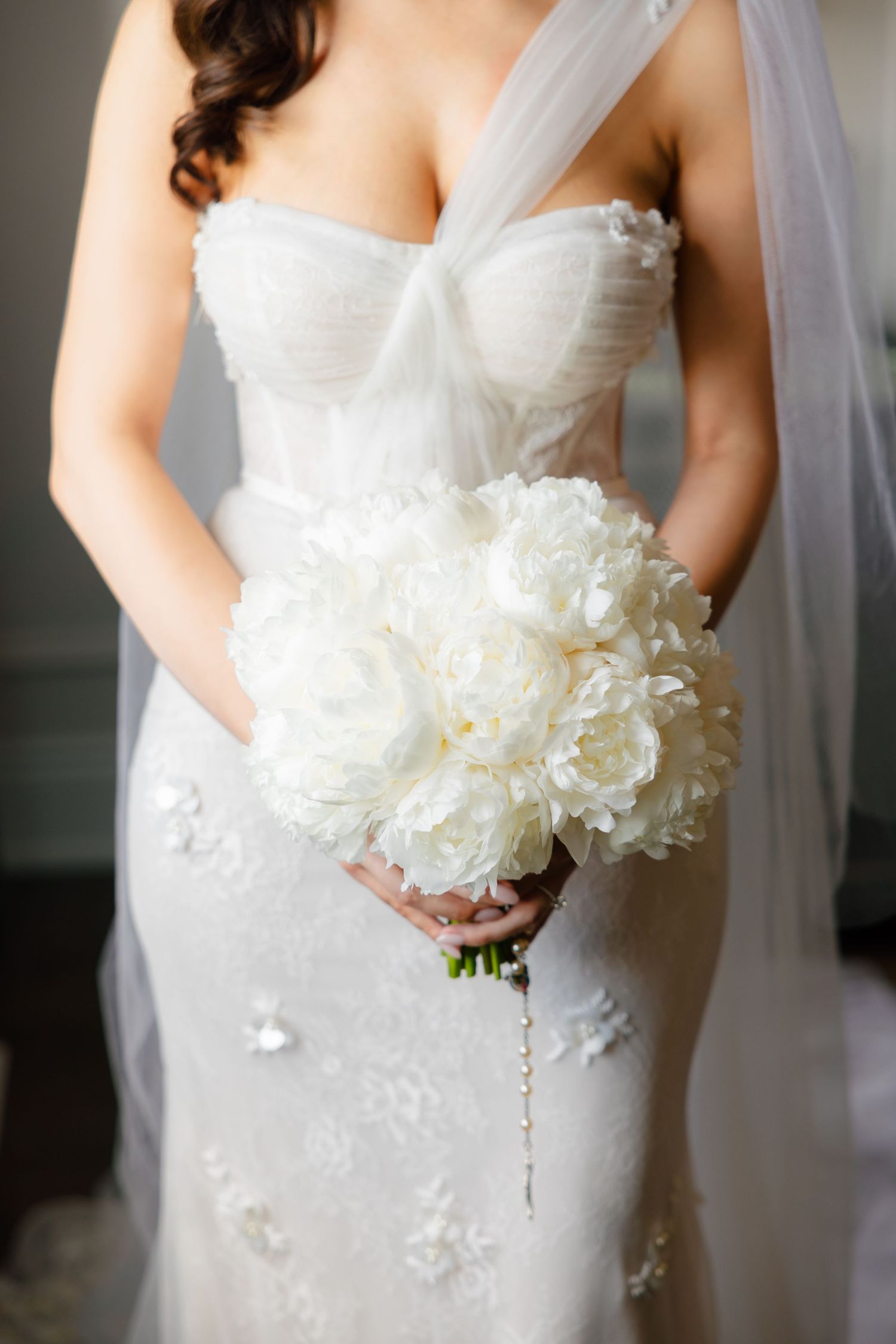 Close up of wedding dress bodice and white peony bouquet with delicate details.
