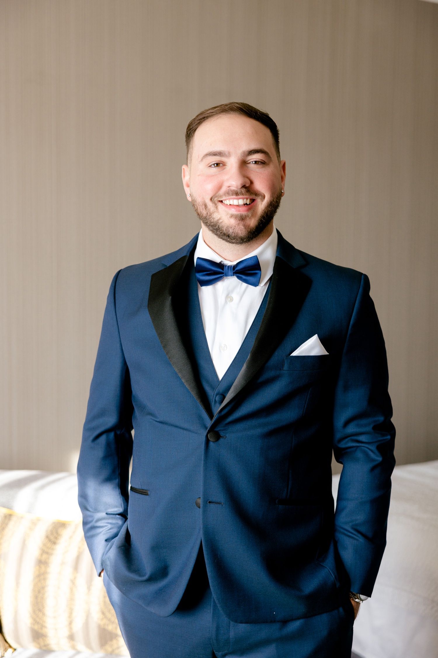 A formal portrait of someone wearing a navy blue tuxedo with black lapels and blue bow tie.