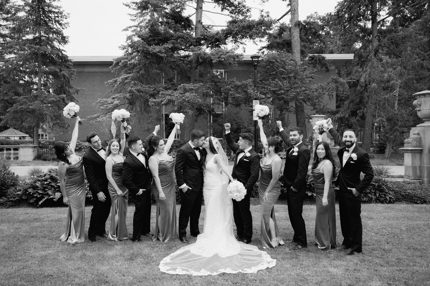 Black and white photo of wedding party jumping and celebrating outdoors.