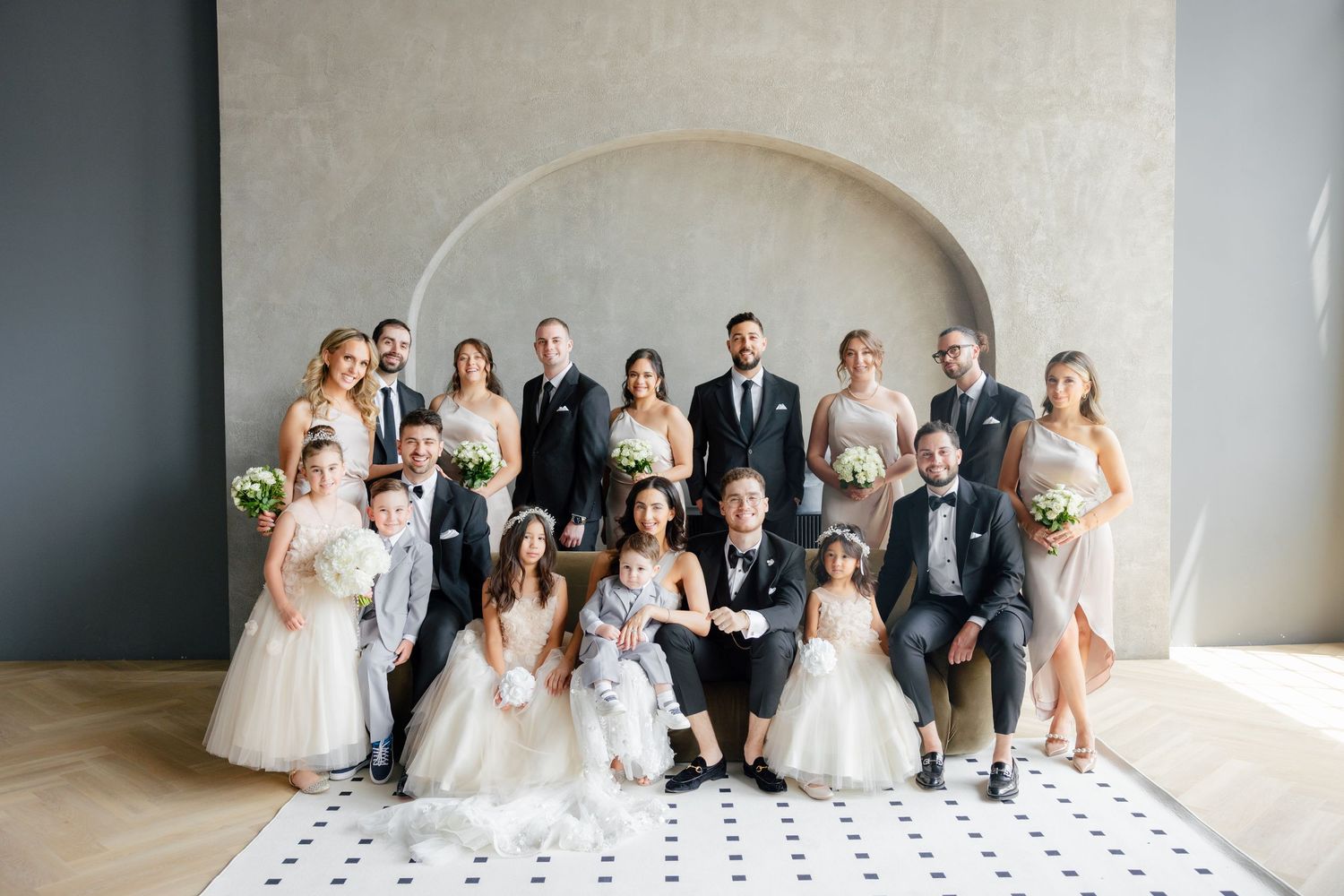 Wedding party poses together under arched wall for formal group photo.