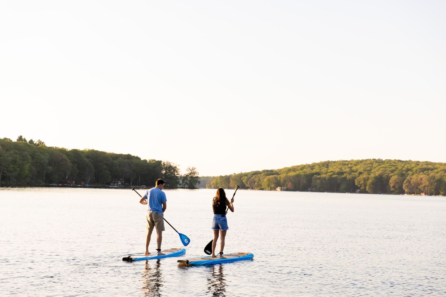Couple paddleboarding together on peaceful lake during sunset.
