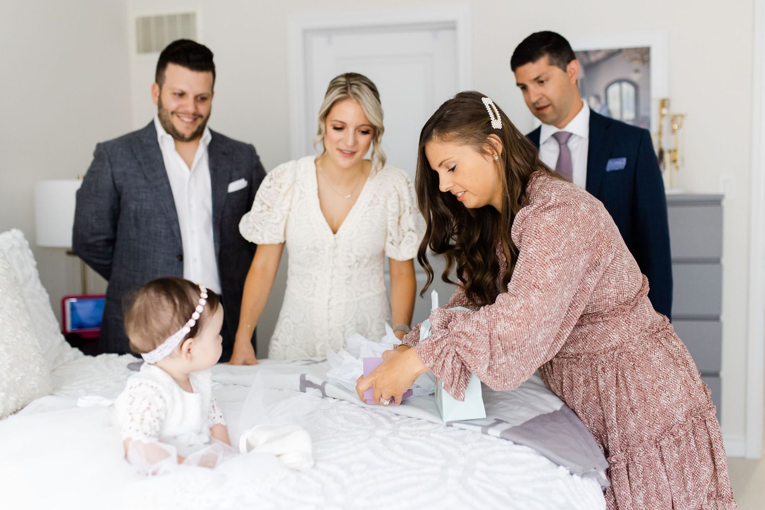 Family gathering around baby on white bed during special occasion photoshoot.