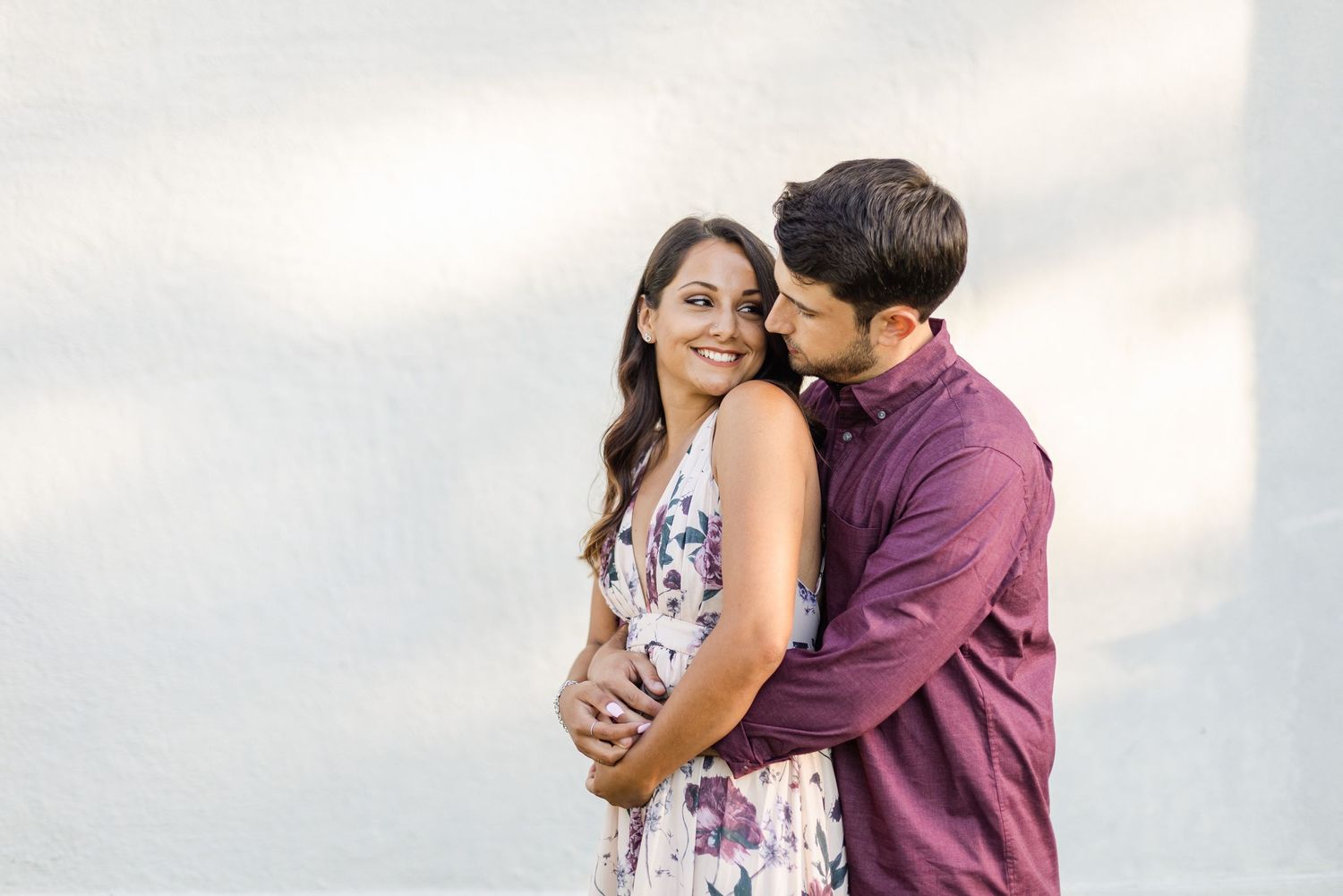 Intimate portrait of couple embracing against sunlit white architectural background.
