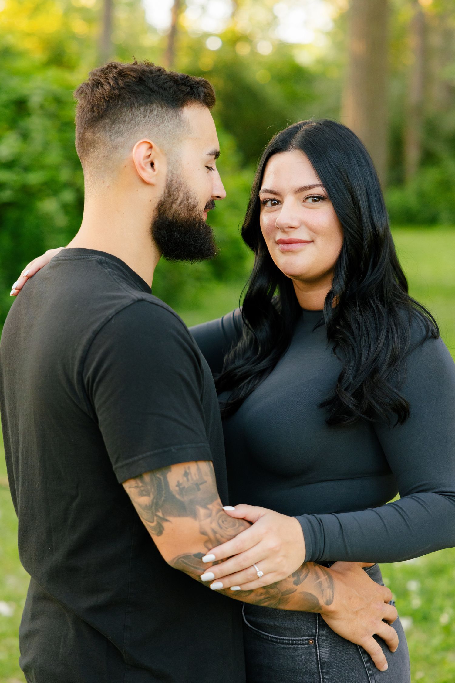 Couple in coordinated black outfits sharing a romantic moment in a sunlit park.