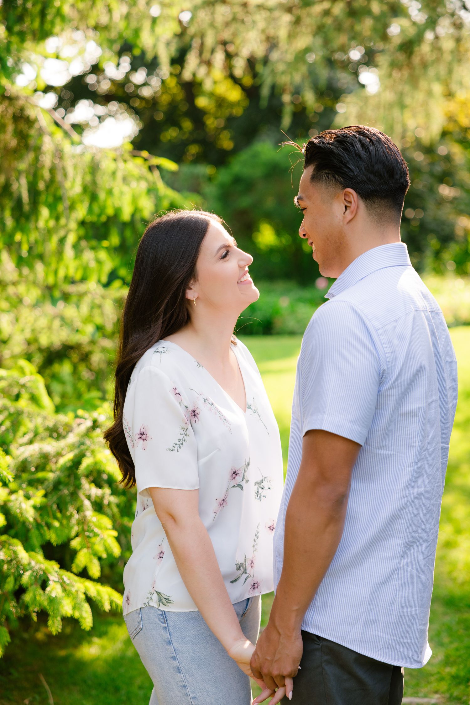 A couple shares an affectionate moment while holding hands in front of evergreen trees.