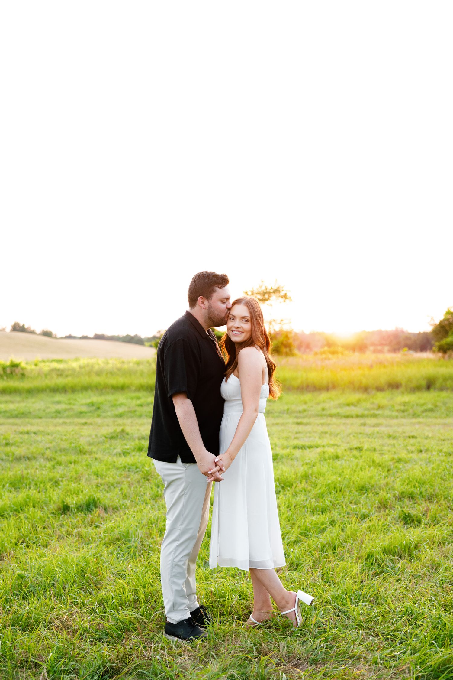 A couple share an intimate moment in a sunlit field at sunset wearing black and white outfits.