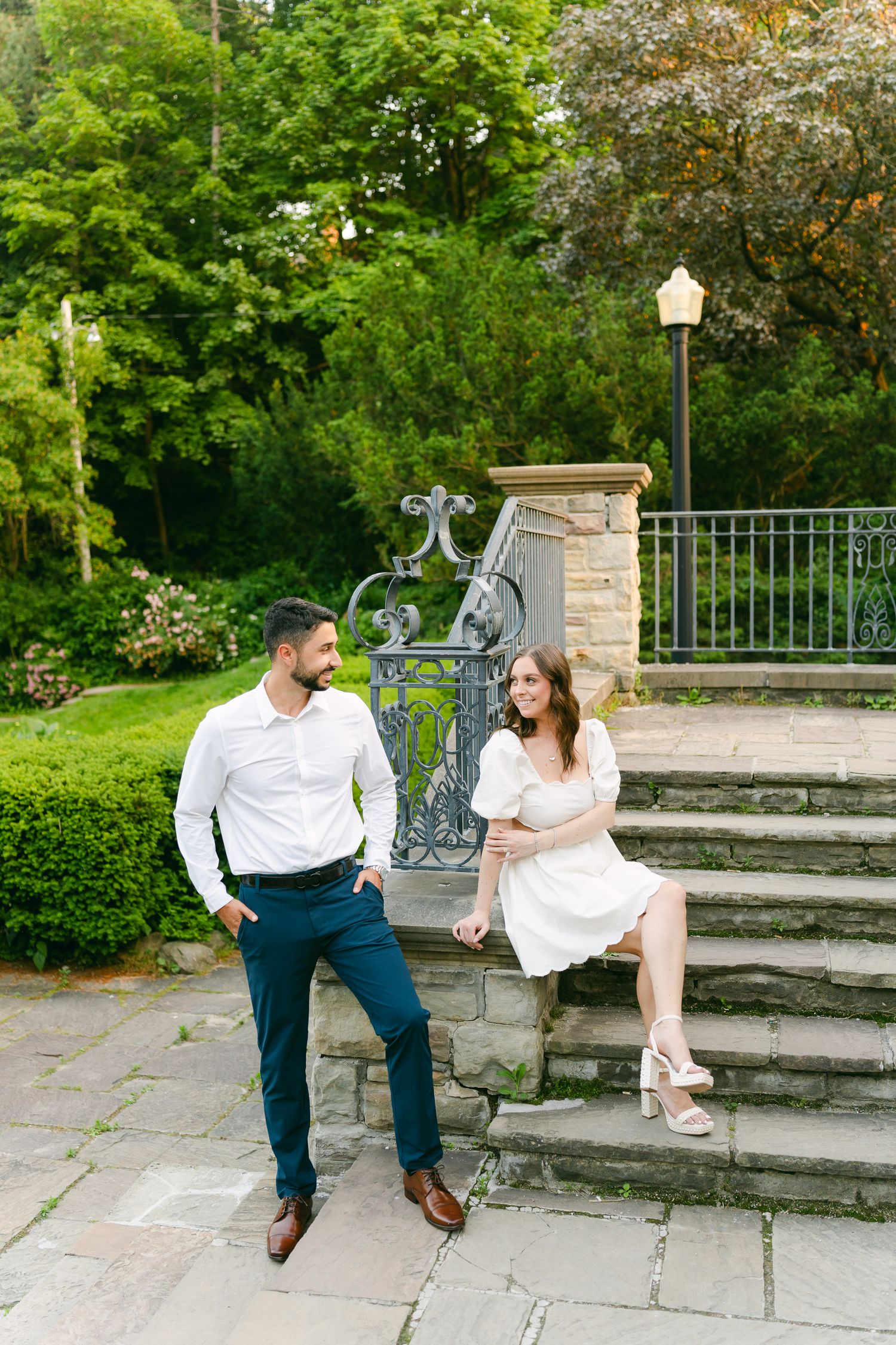 Two people share a candid moment while sitting on outdoor stone steps near decorative metalwork.
