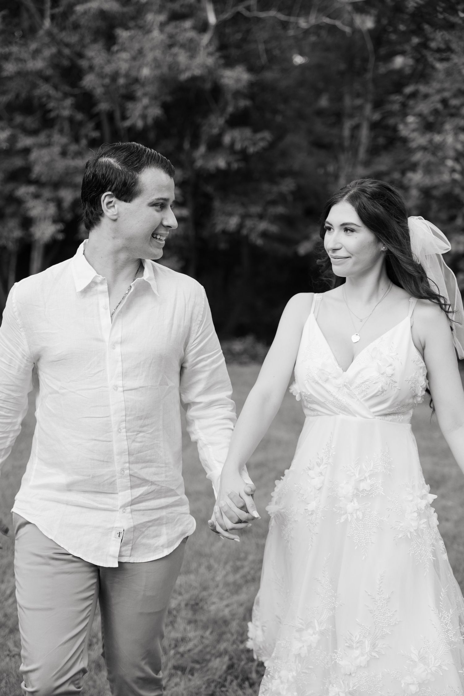 A black and white photo of newlyweds walking hand in hand through a garden.
