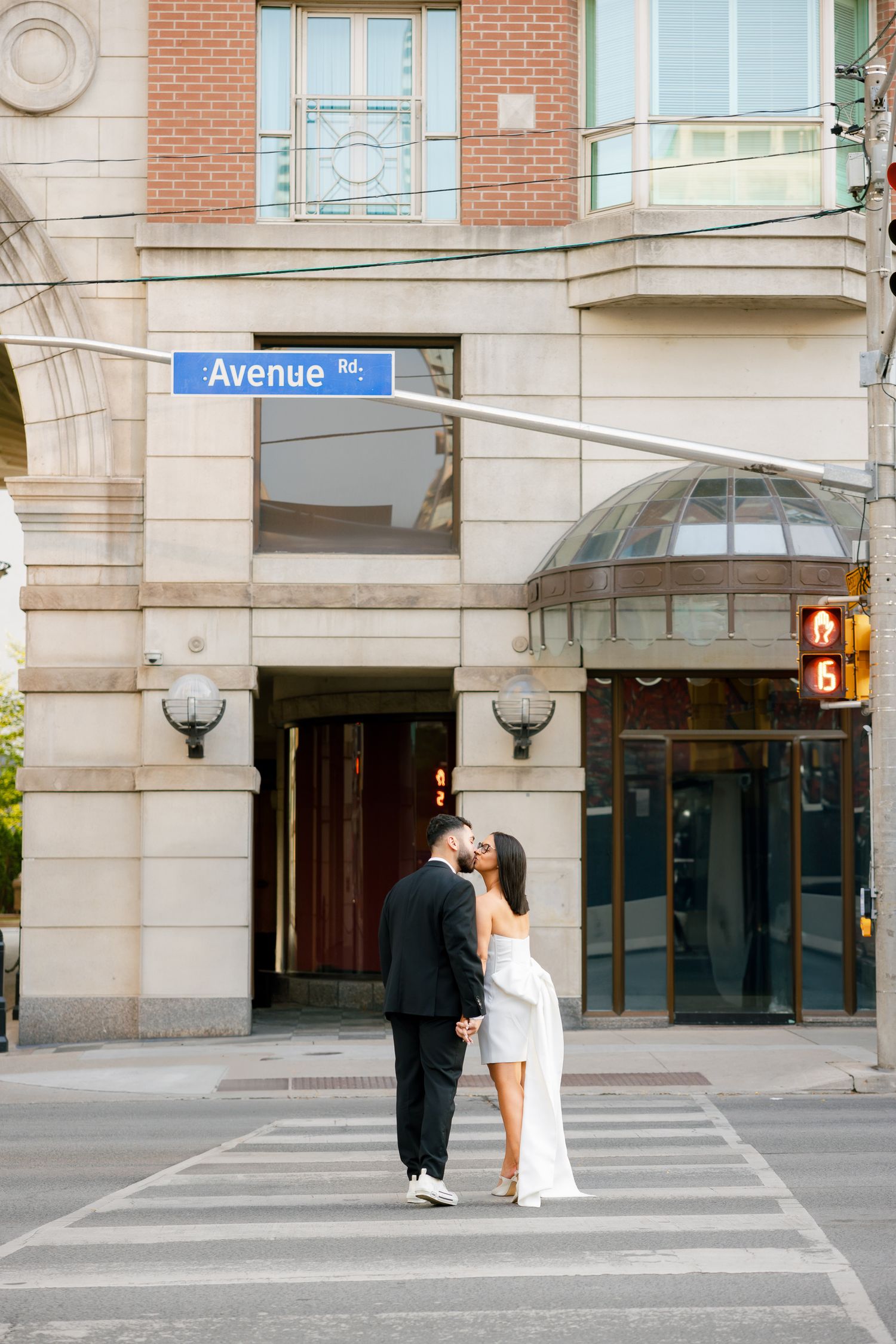 A couple sharing an intimate moment on a crosswalk in front of a building with Avenue signage.