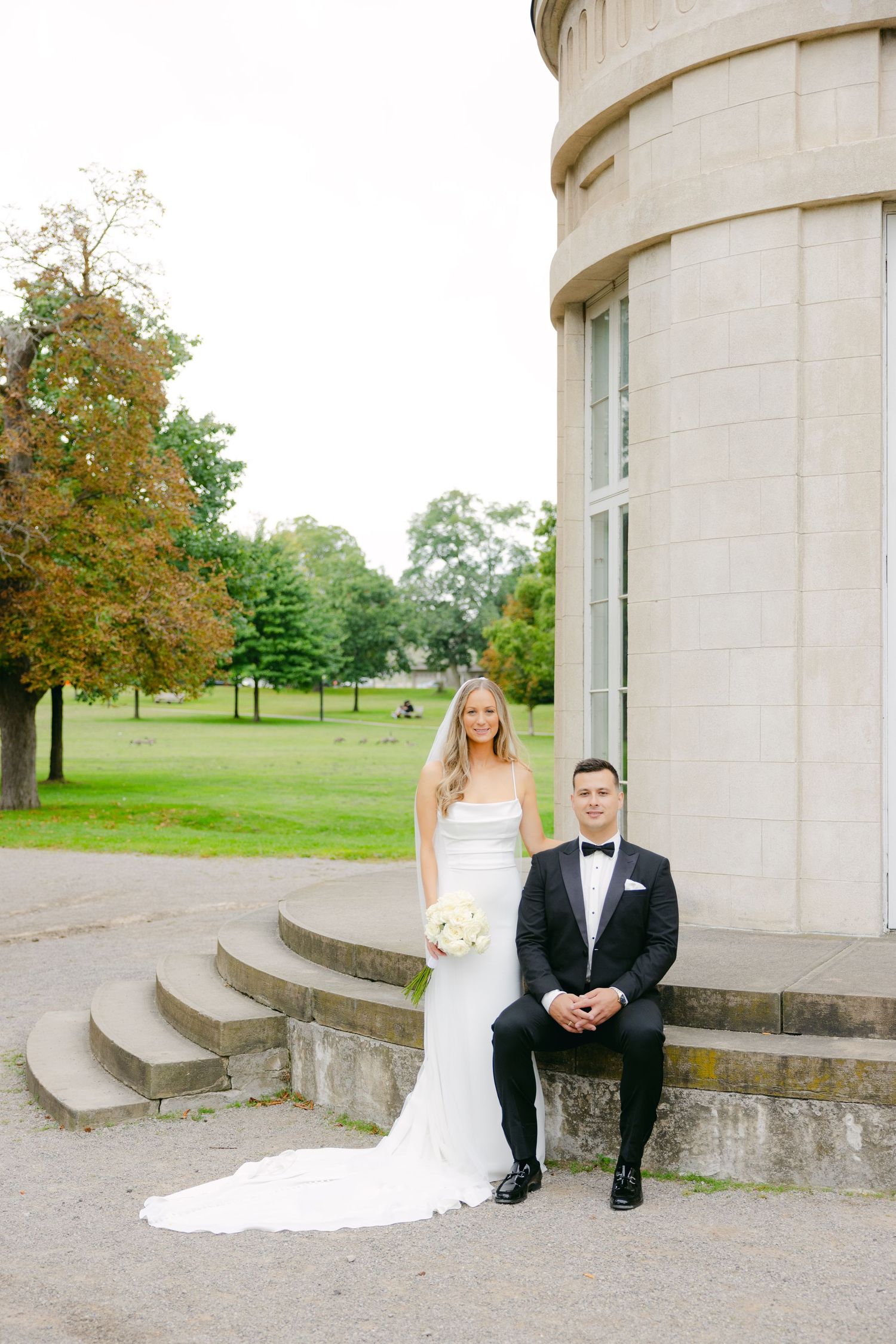 Newlyweds pose together on stone steps of grand circular tower building.