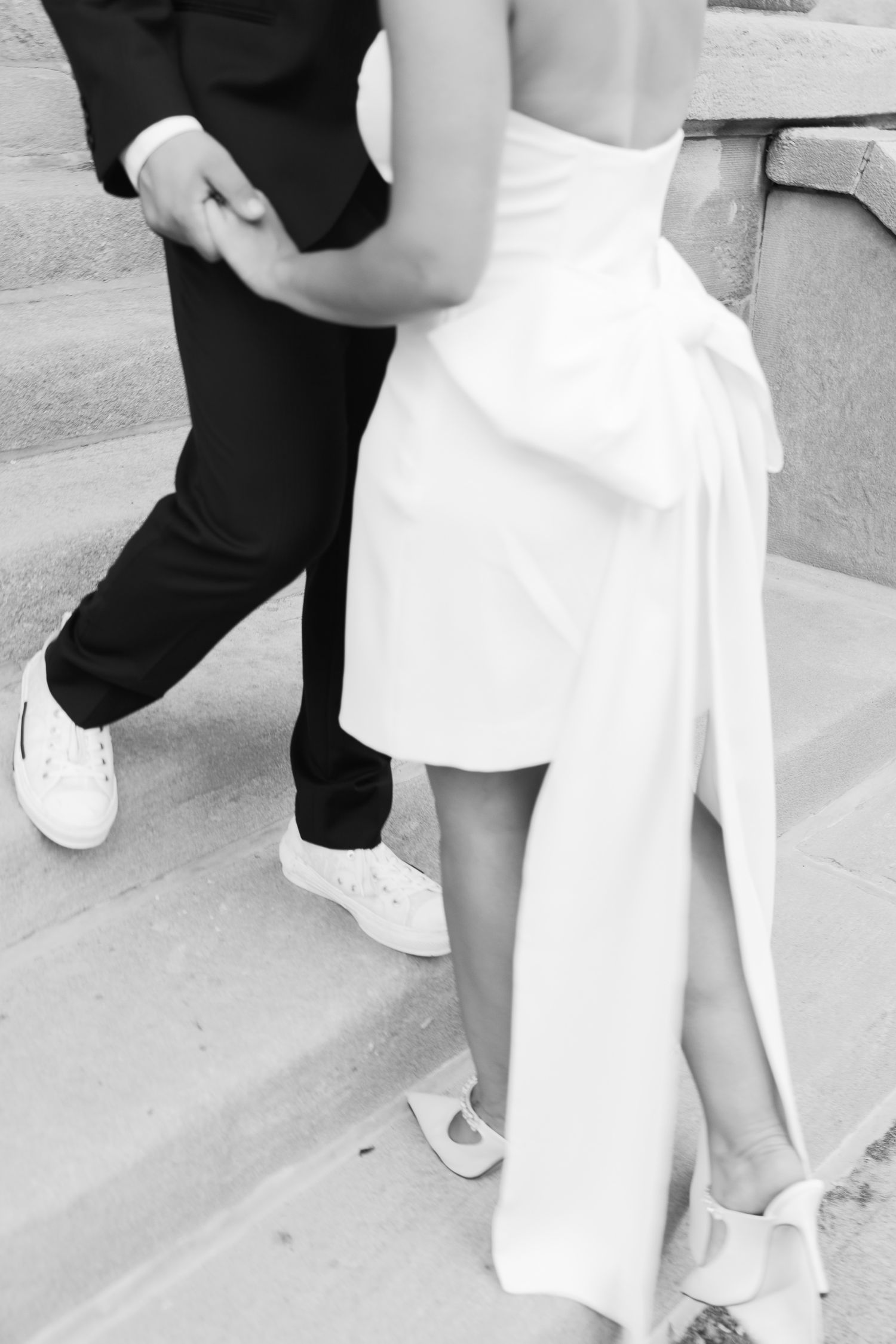 Detail shot of formal attire and white sneakers as couple embraces on steps.