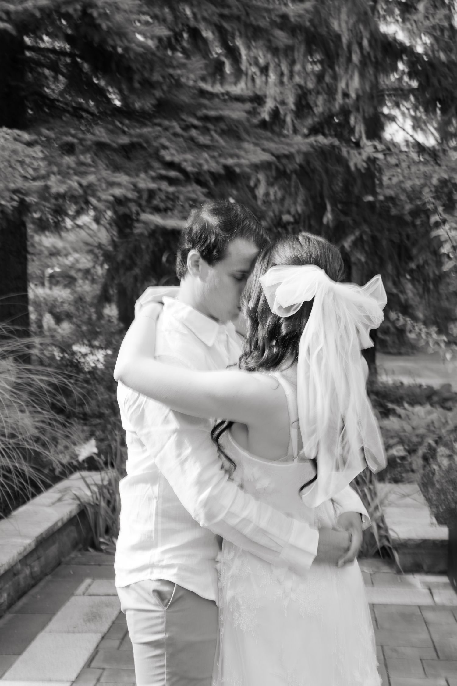 A black and white portrait of a romantic embrace between newlyweds on a stone patio.