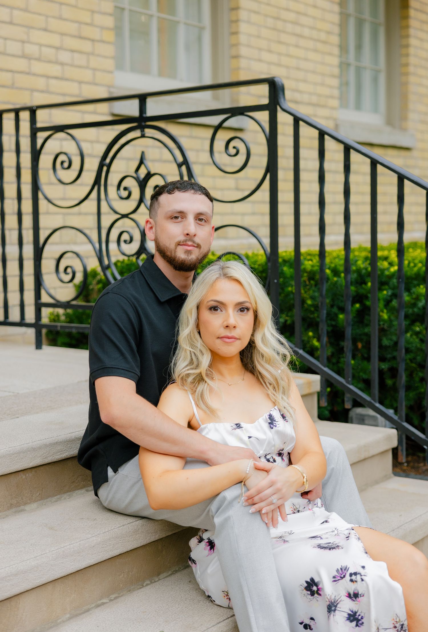 A romantic portrait shot of a couple sitting on stone steps with decorative black iron railings.