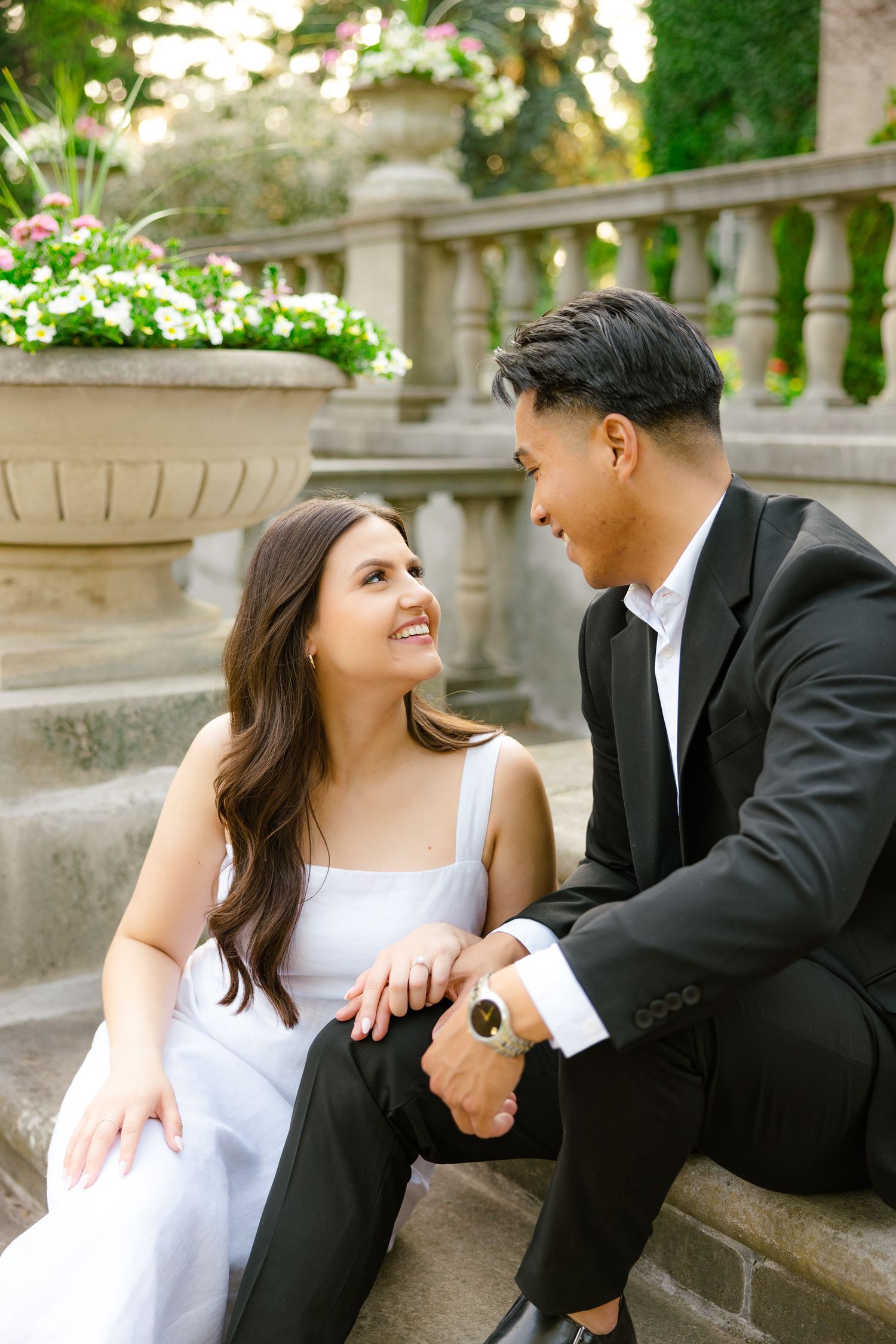 A romantic moment captured on stone steps with decorative planters and classical architecture.