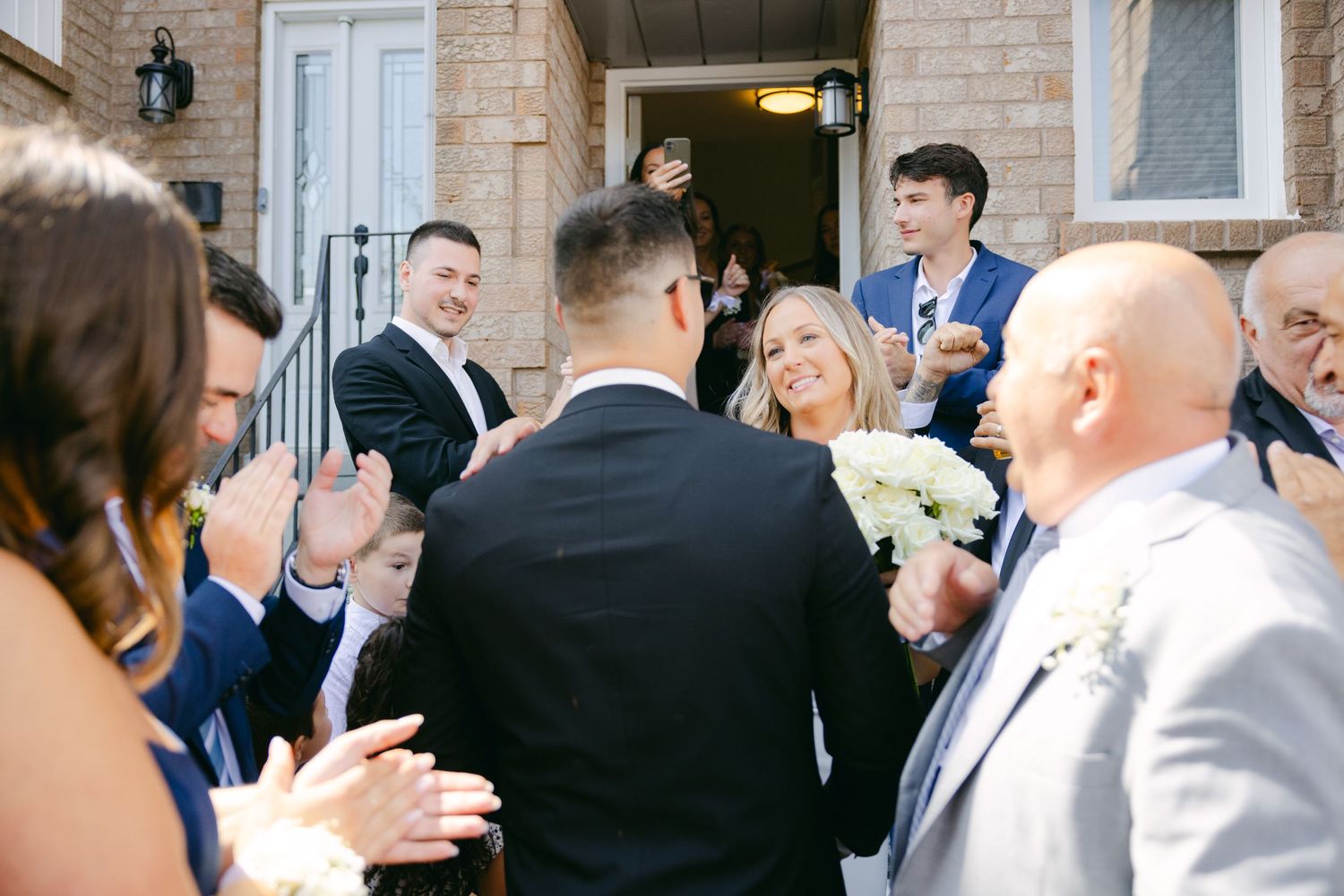 Wedding celebration scene with guests in formal attire outside brick building.