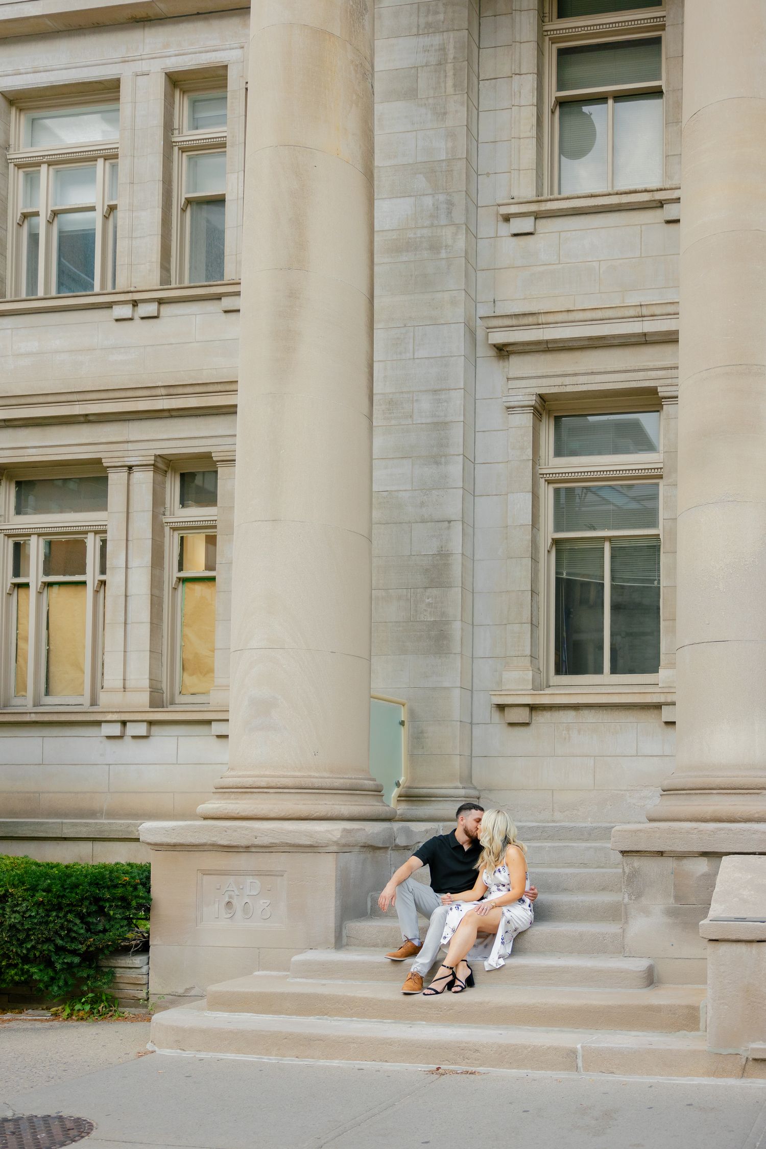 A romantic portrait of a couple seated on steps of a classical building facade.