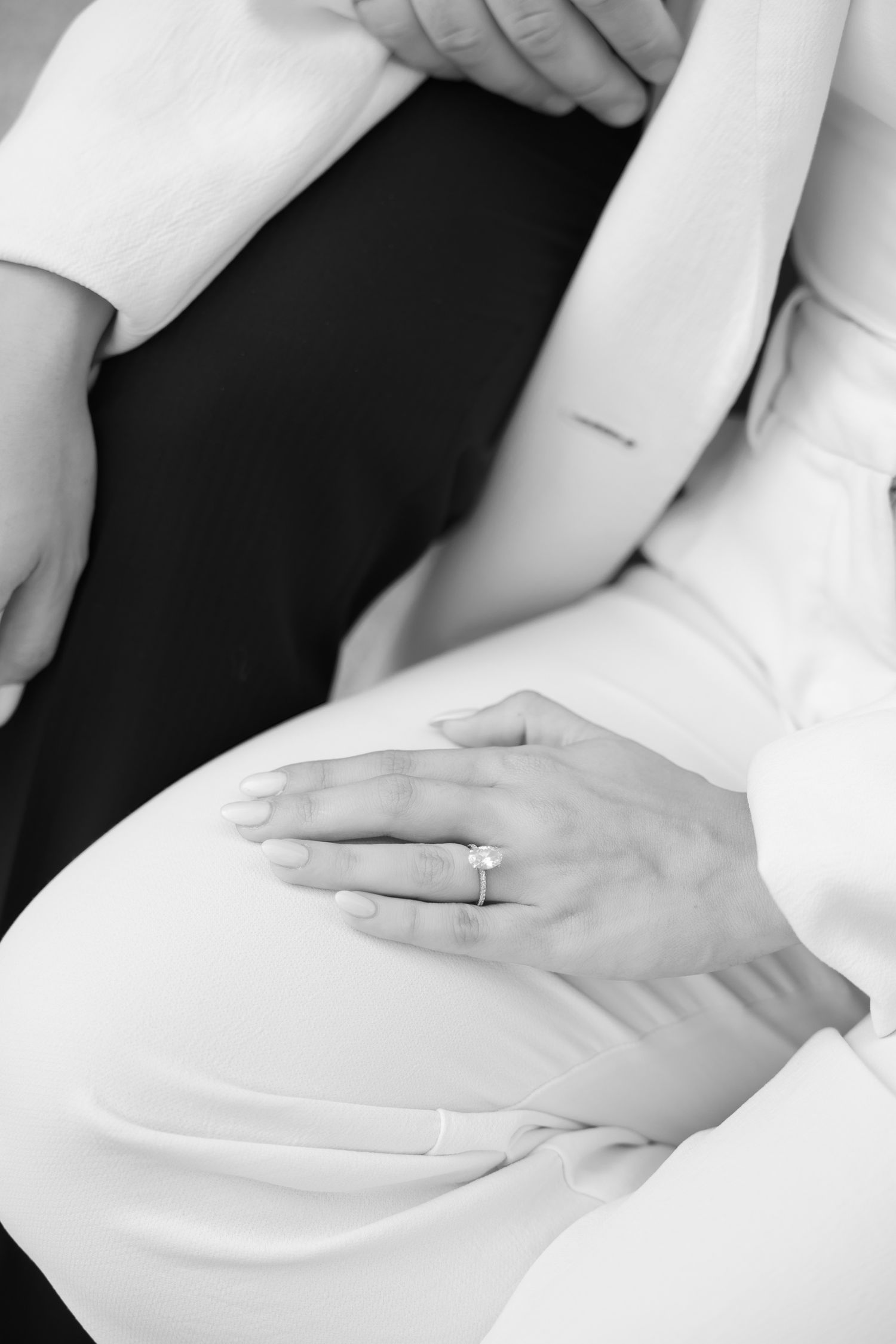 Close-up black and white shot of hands with engagement ring against white fabric.