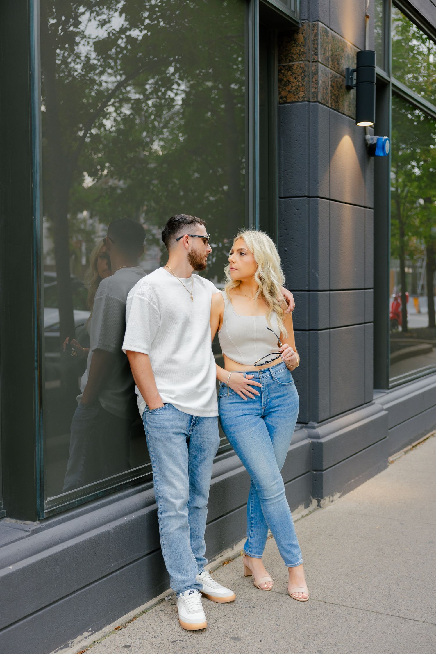 A couple in matching casual wear standing against a modern storefront wall.