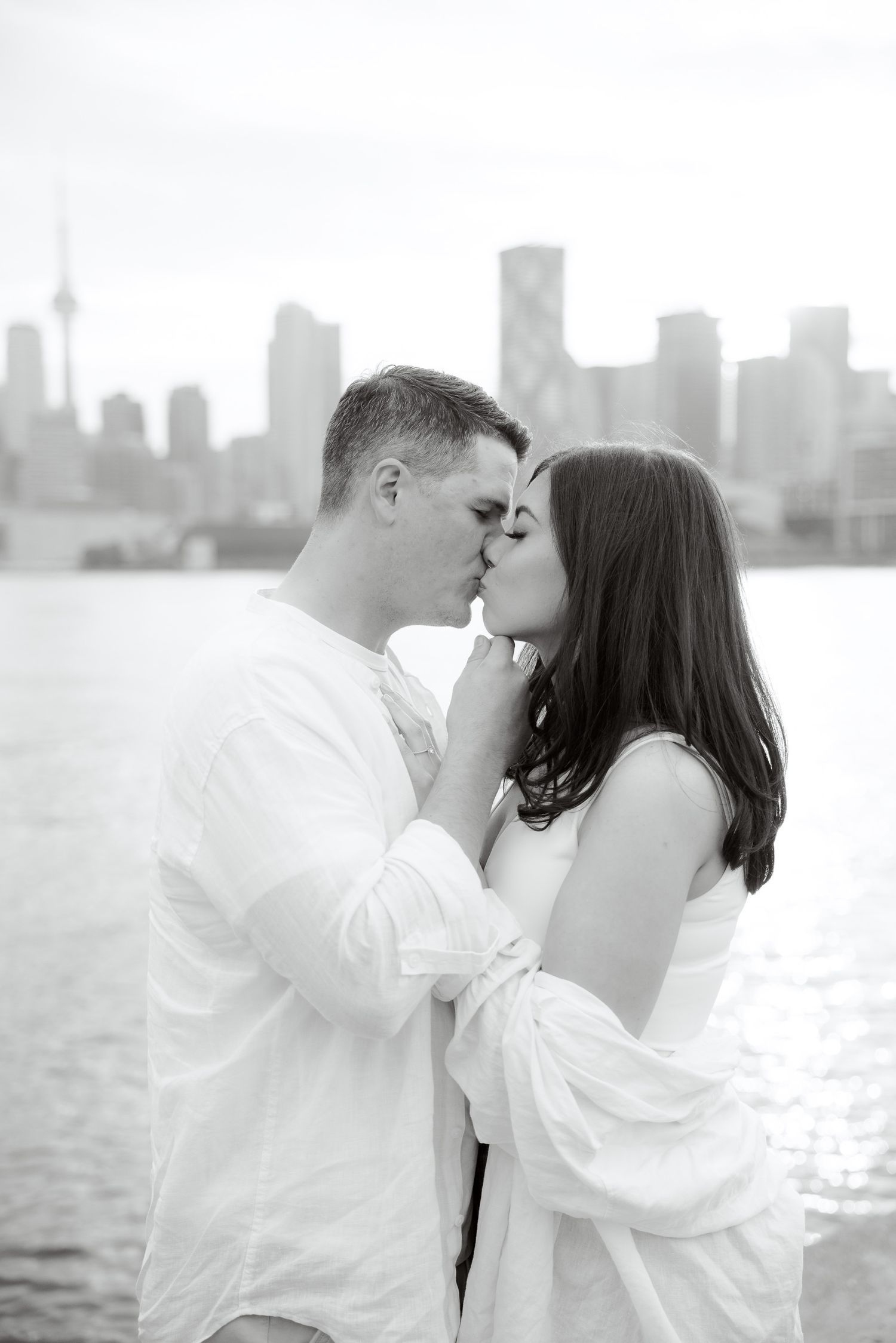A black and white portrait of a tender kiss with a dramatic city skyline in the background.
