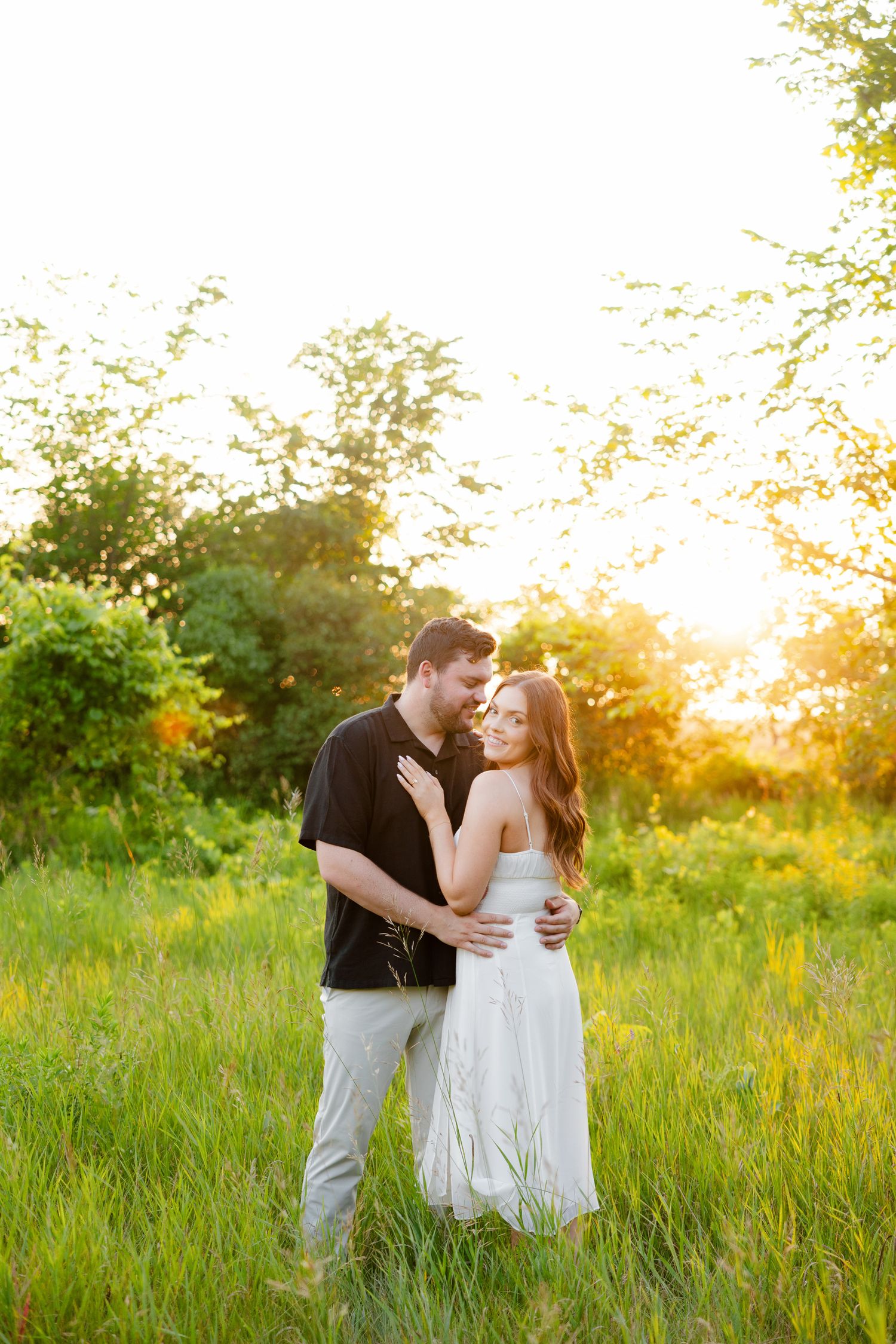 Romantic sunset portrait of couple standing in meadow with warm golden light.