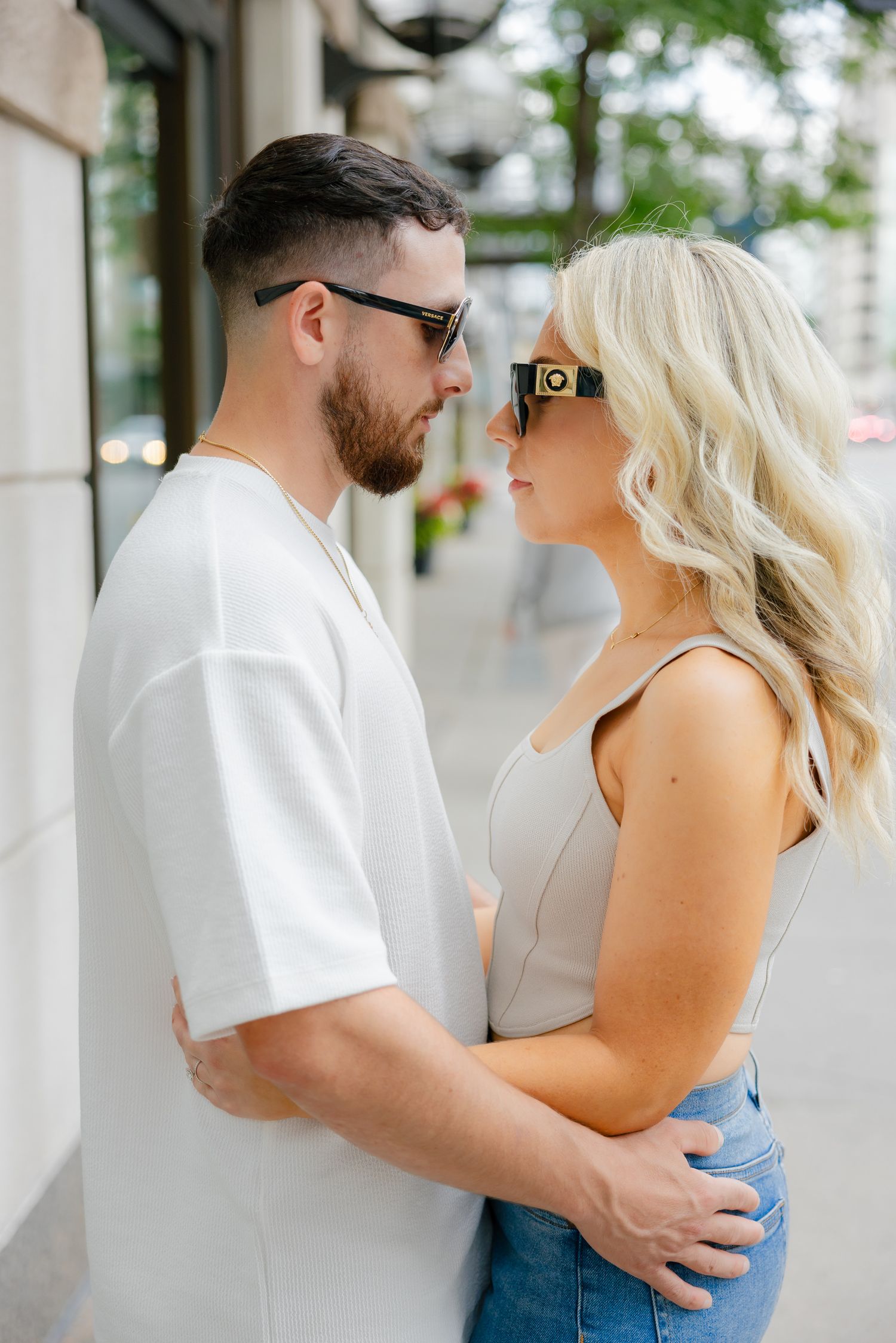 A romantic couple in casual attire sharing an intimate moment outside a storefront.