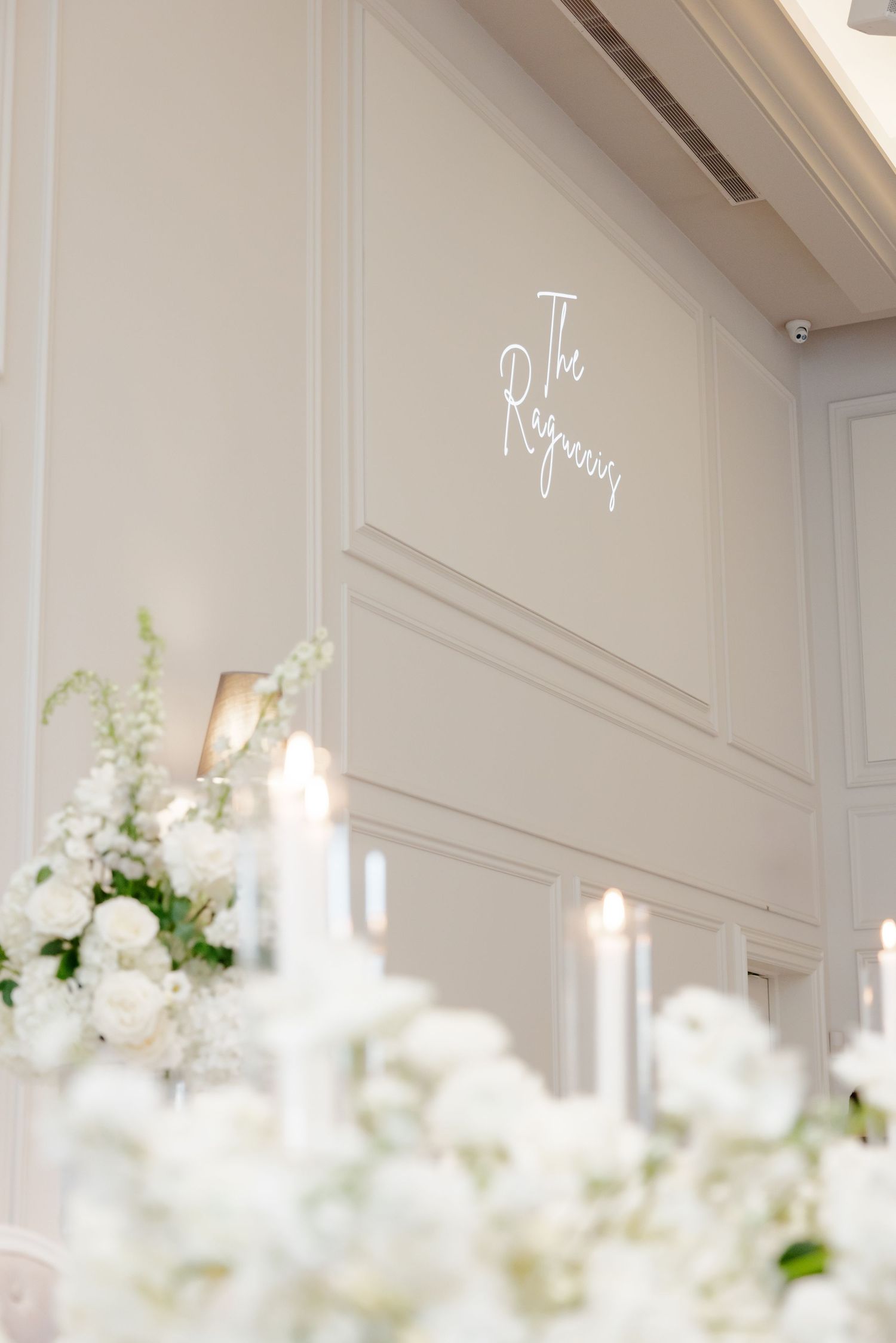 White neon sign reading 'The Regency' mounted on light gray wall above floral arrangements and candles.