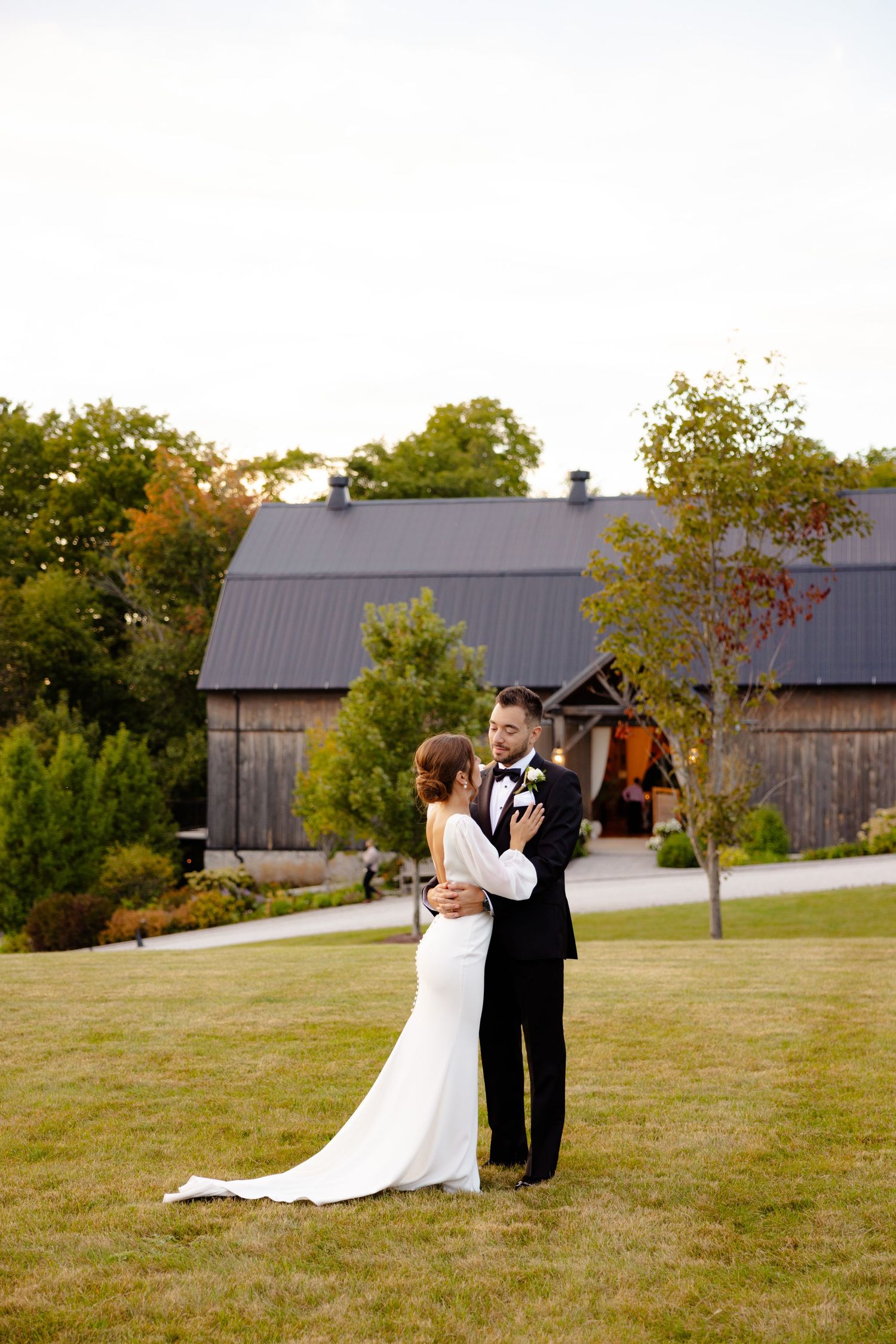 A couple shares an intimate embrace on their wedding day with a rustic barn in the background.